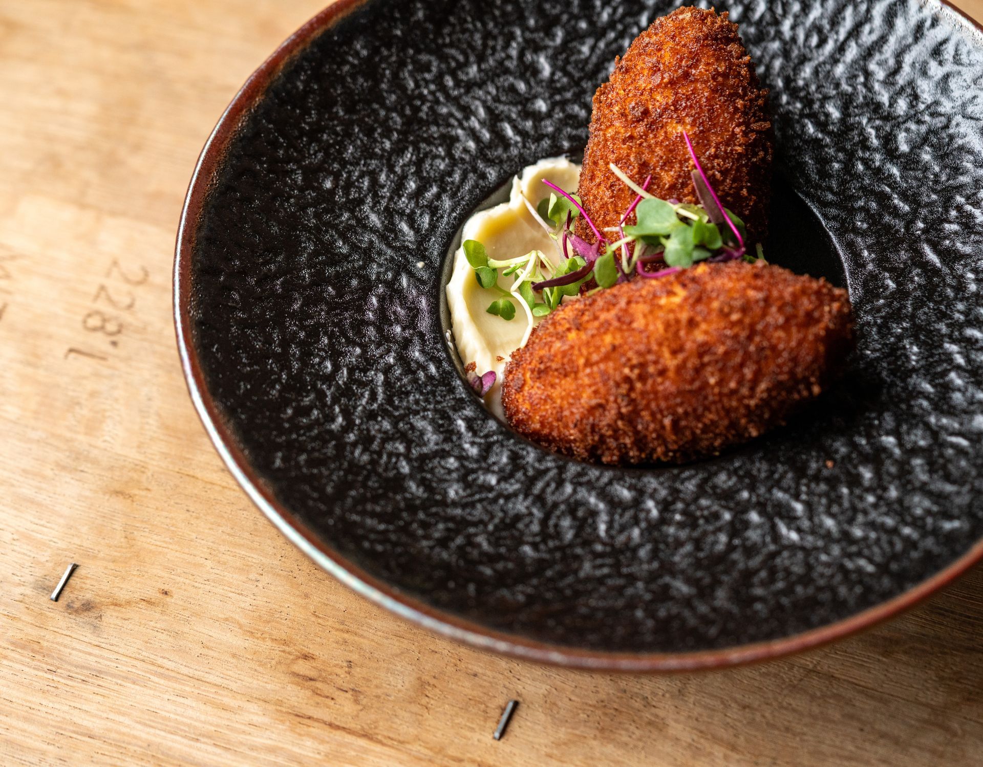 Two breaded croquettes on a plate with mashed food and microgreens.
