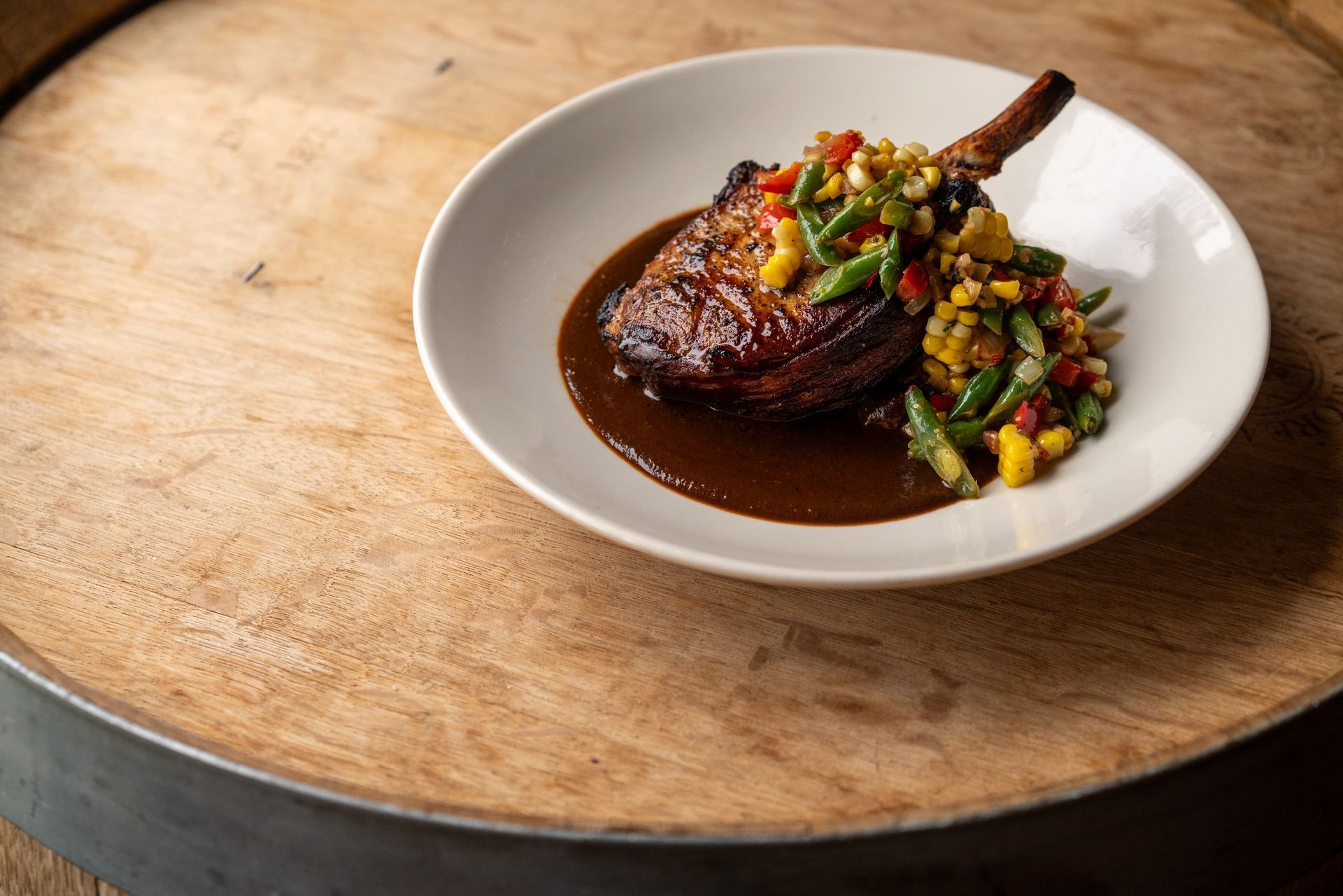 Pork chop with sauce and colorful relish on a white plate atop a wooden surface.