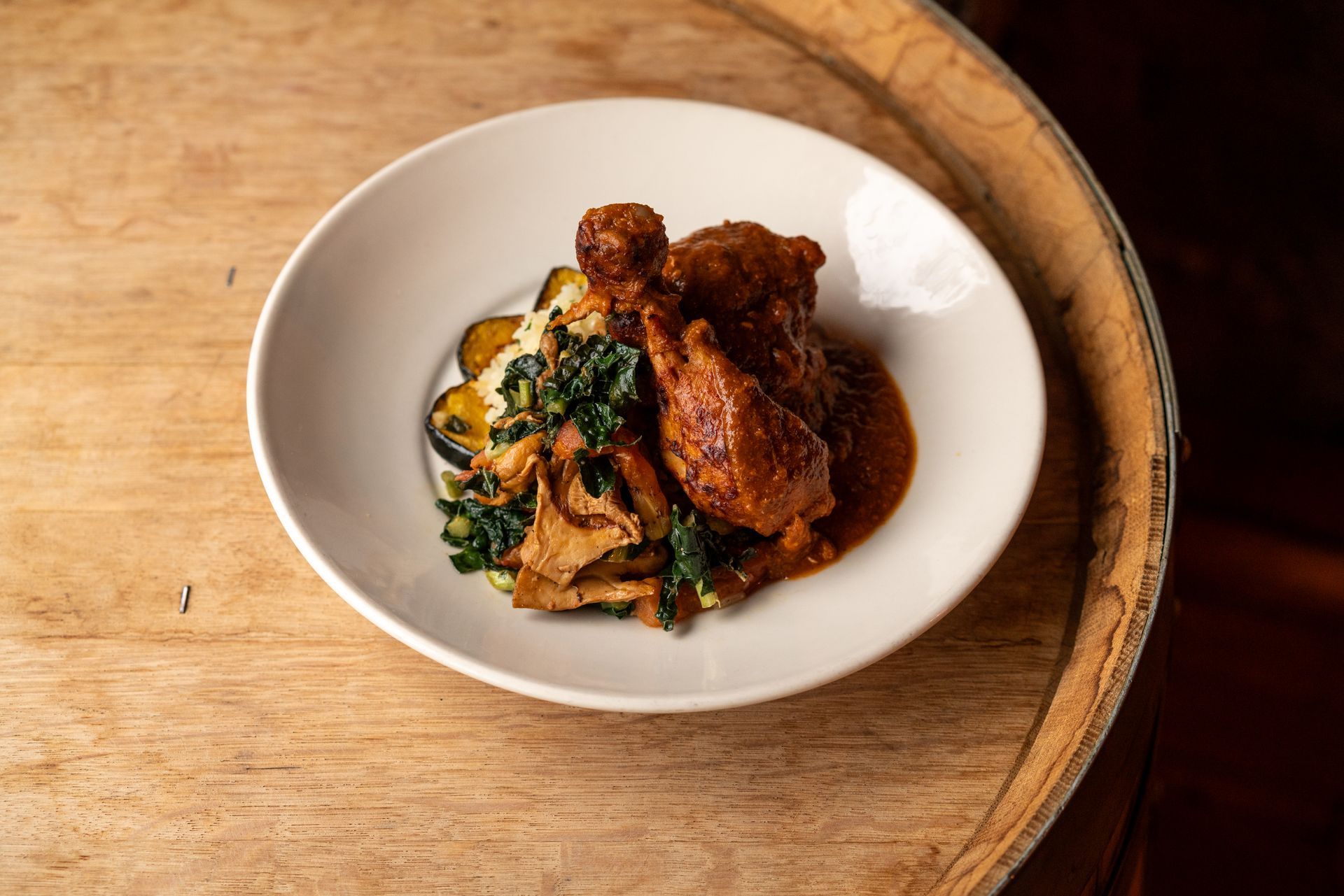 Plate of food with chicken in sauce, vegetables, and potatoes, on a wooden surface.