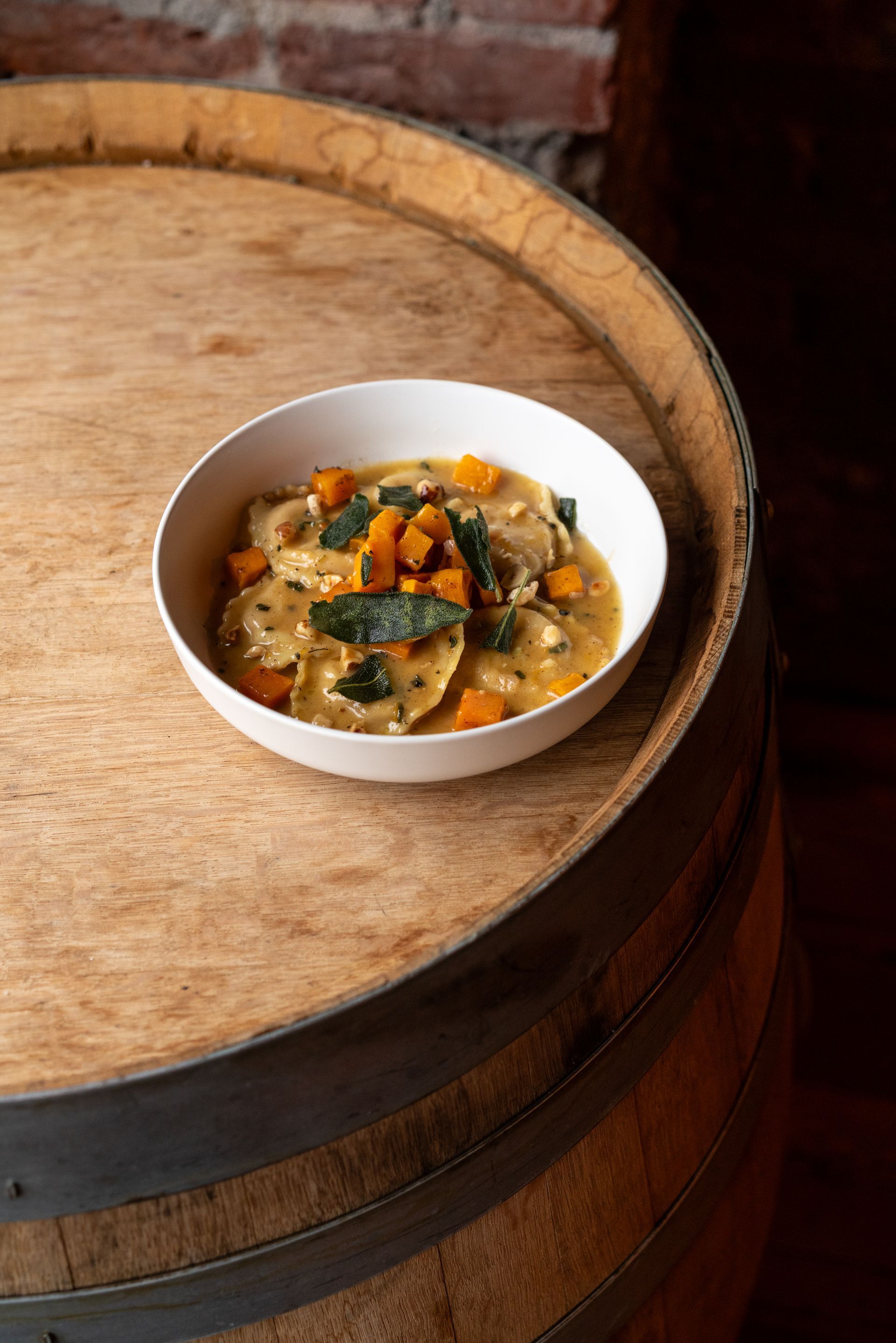 Bowl of ravioli with squash and sage on a wooden barrel.
