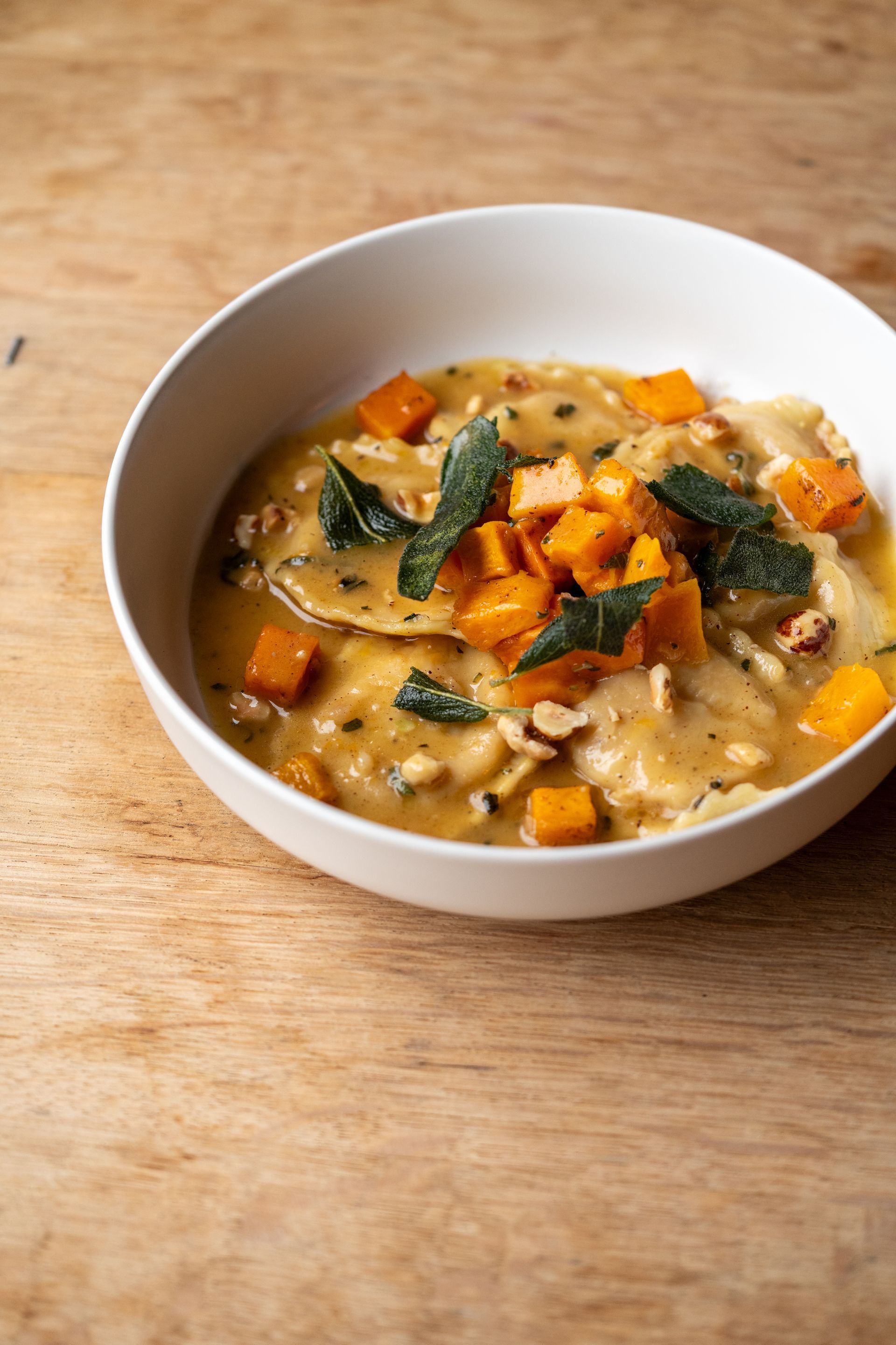 Butternut squash ravioli with sage and nuts in a white bowl on a wooden surface.