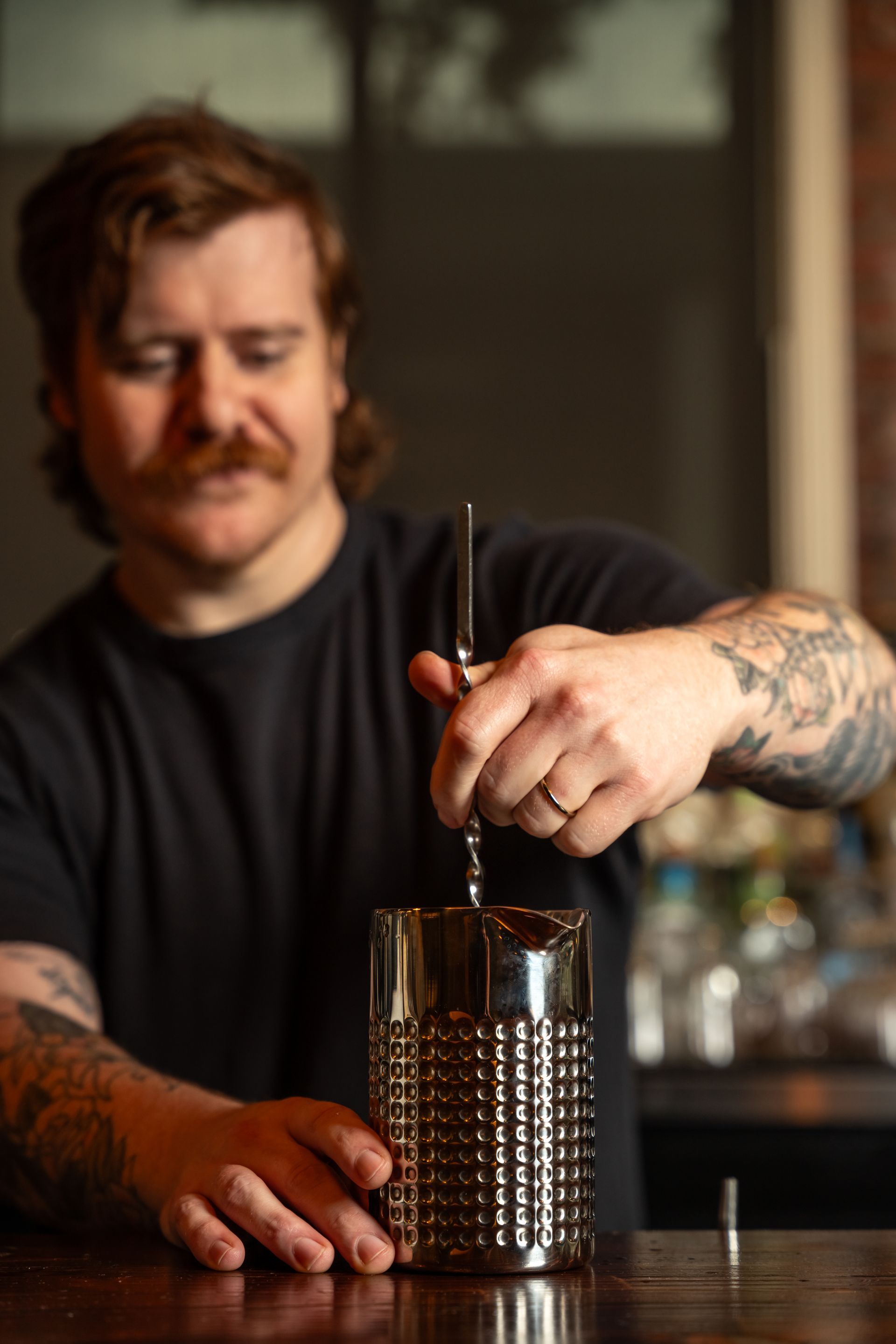 A bartender mixing a drink in a textured silver glass, inside a bar.