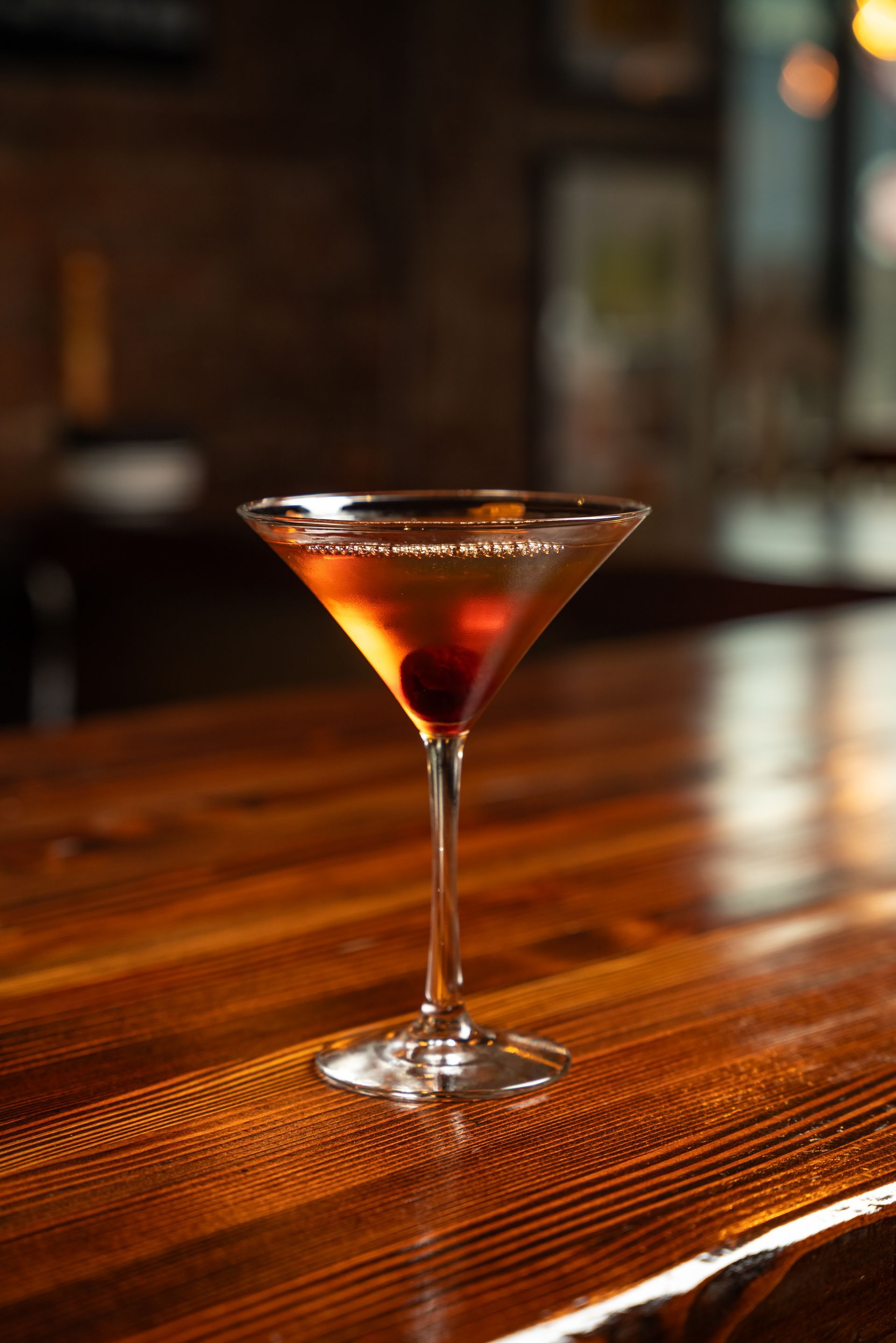 Cocktail in a martini glass, with a cherry, on a wooden bar.