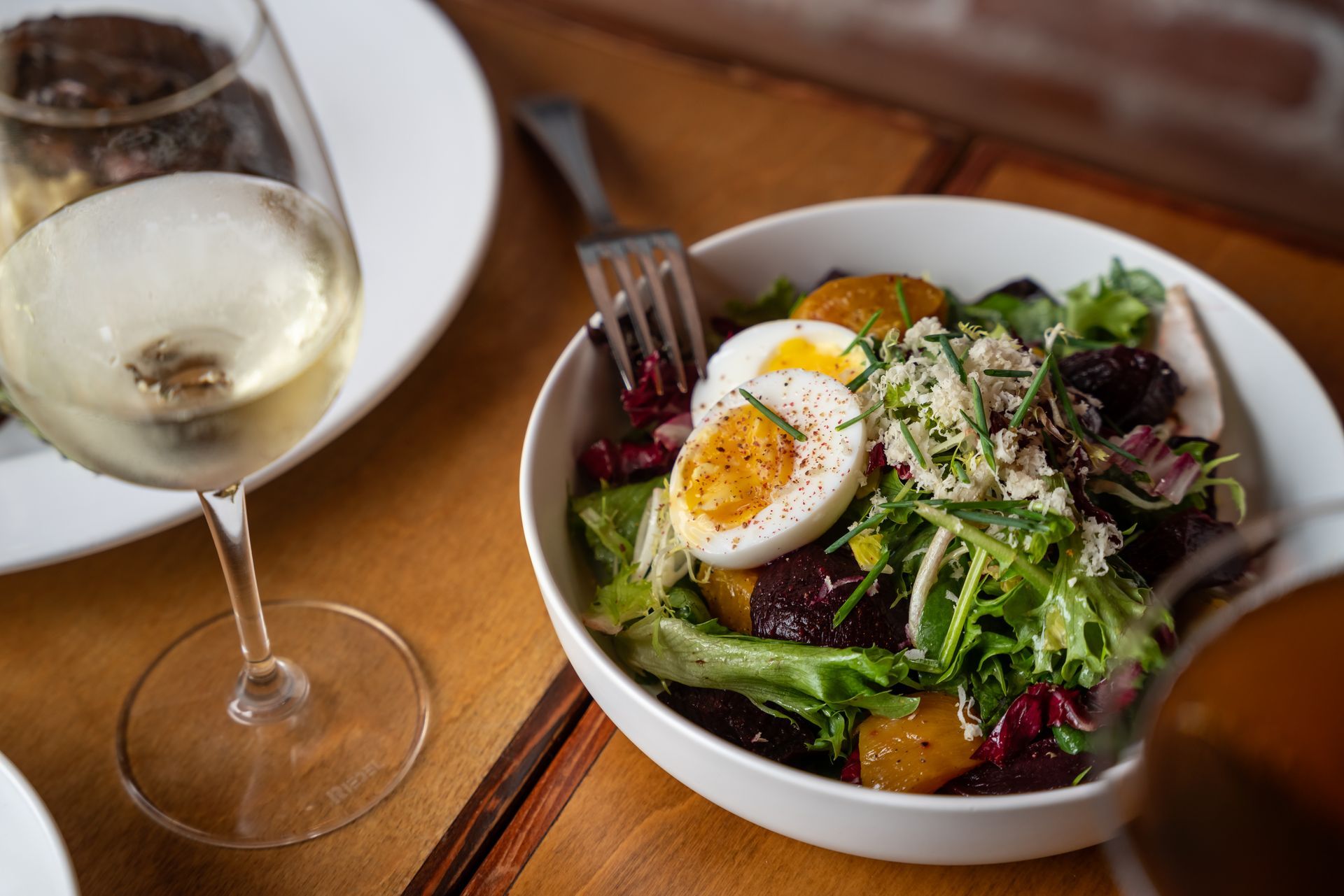 Salad with beets, egg, greens, wine glass, wooden table.