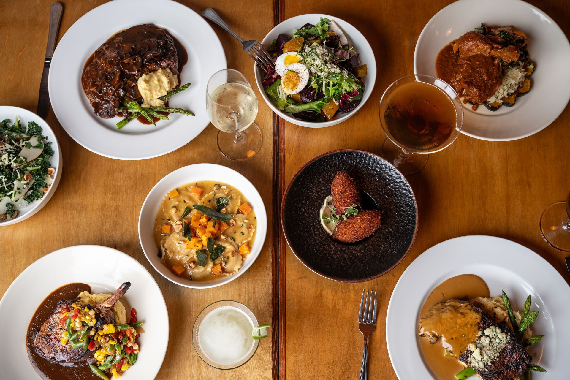 Overhead shot of a wooden table with various plated dishes, drinks, and utensils, showcasing a dining experience.