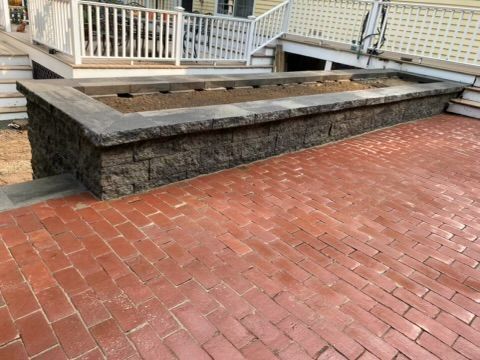 Brick patio with a raised stone planter and white railing beside a building