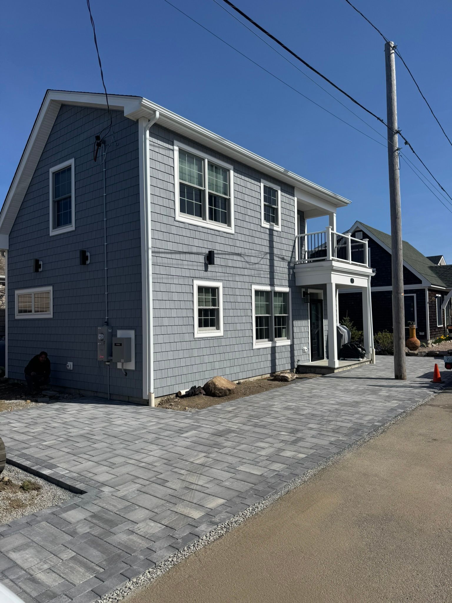 Gray two-story house with white trim, driveway pavers, and a small porch under a blue sky