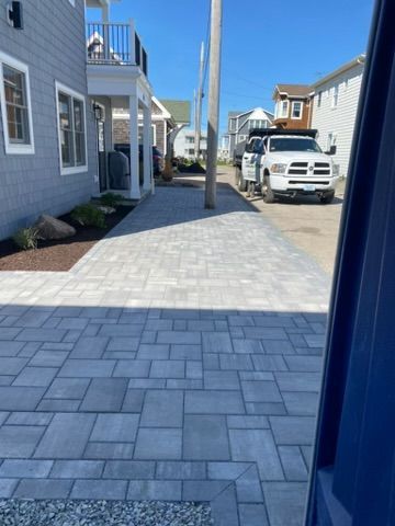 Paved driveway walkway between blue houses, with a white pickup truck parked ahead.