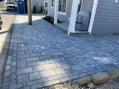 Paved gray stone walkway beside a building, with a utility pole and blue bin in the distance.