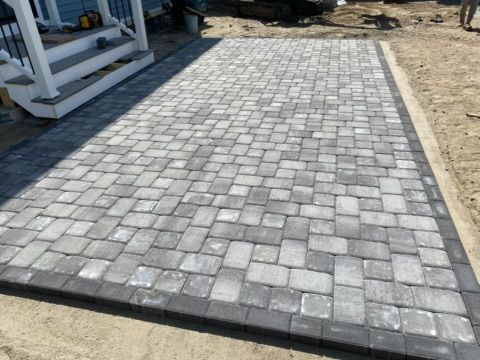 Paved gray stone walkway beside a building, bordered by dirt and white railings.