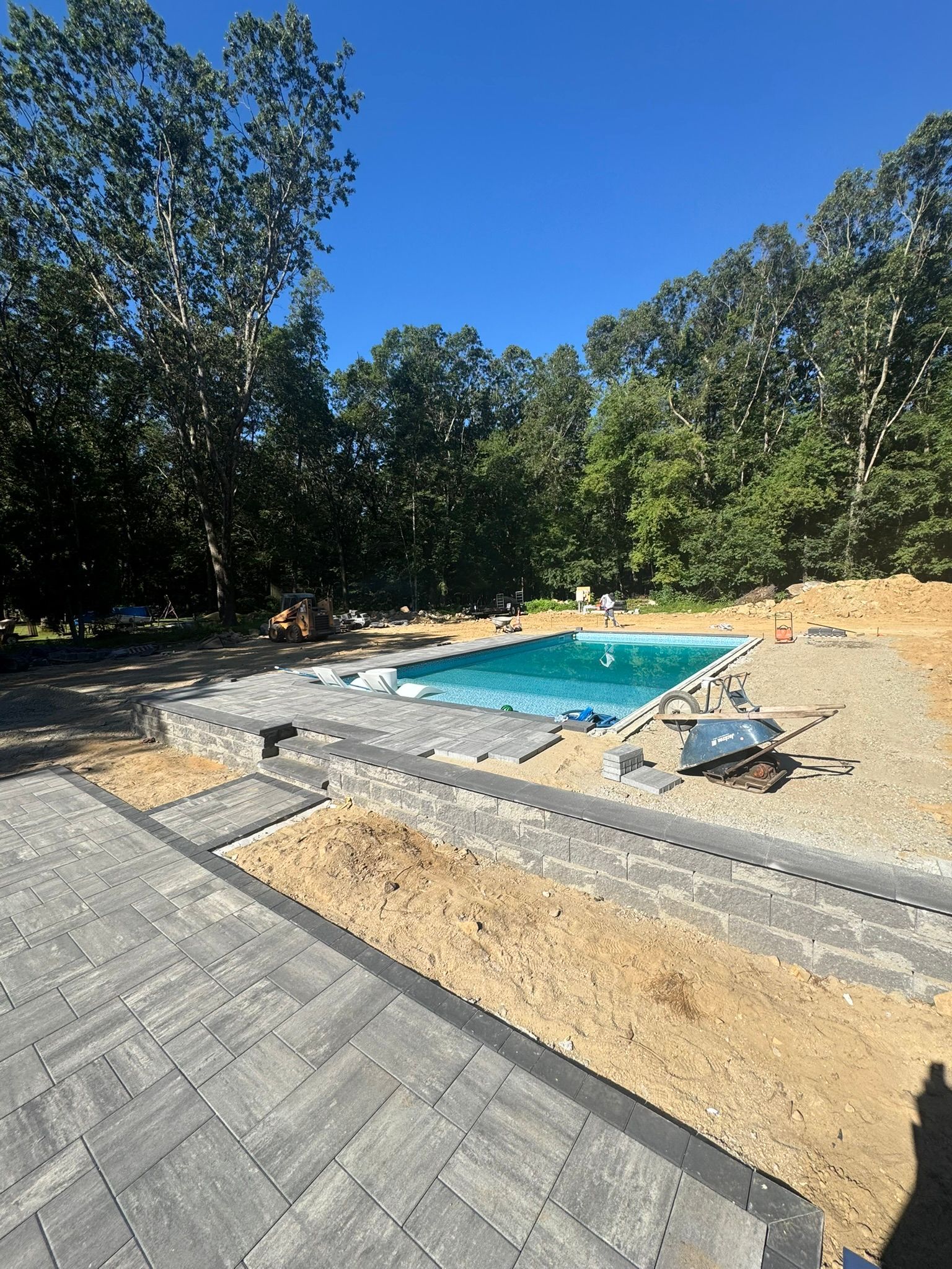 Backyard with a small turquoise pool, paver patio, and dirt landscaping surrounded by trees