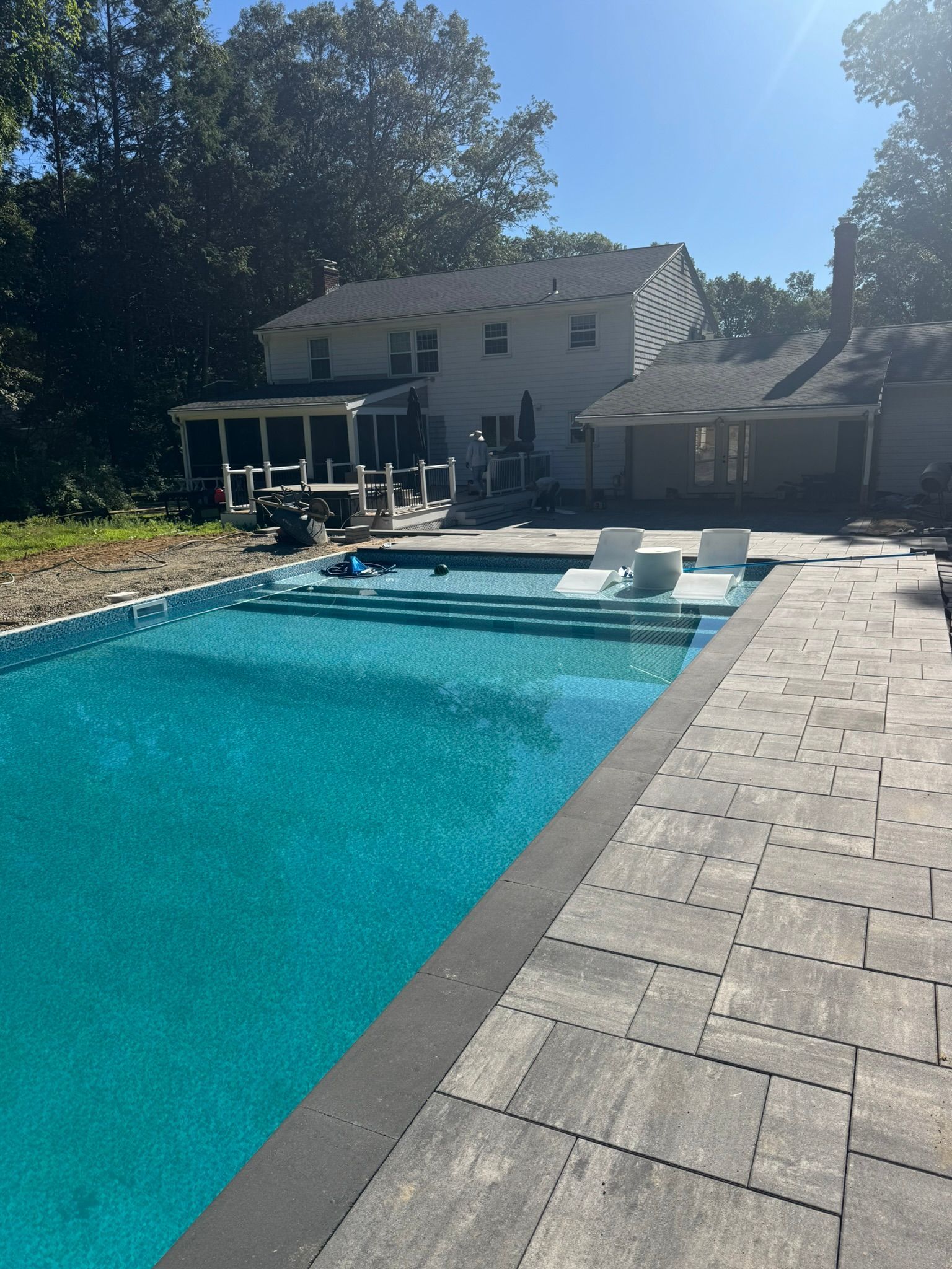 Backyard swimming pool with lounge chairs, patio, and house in bright sunlight