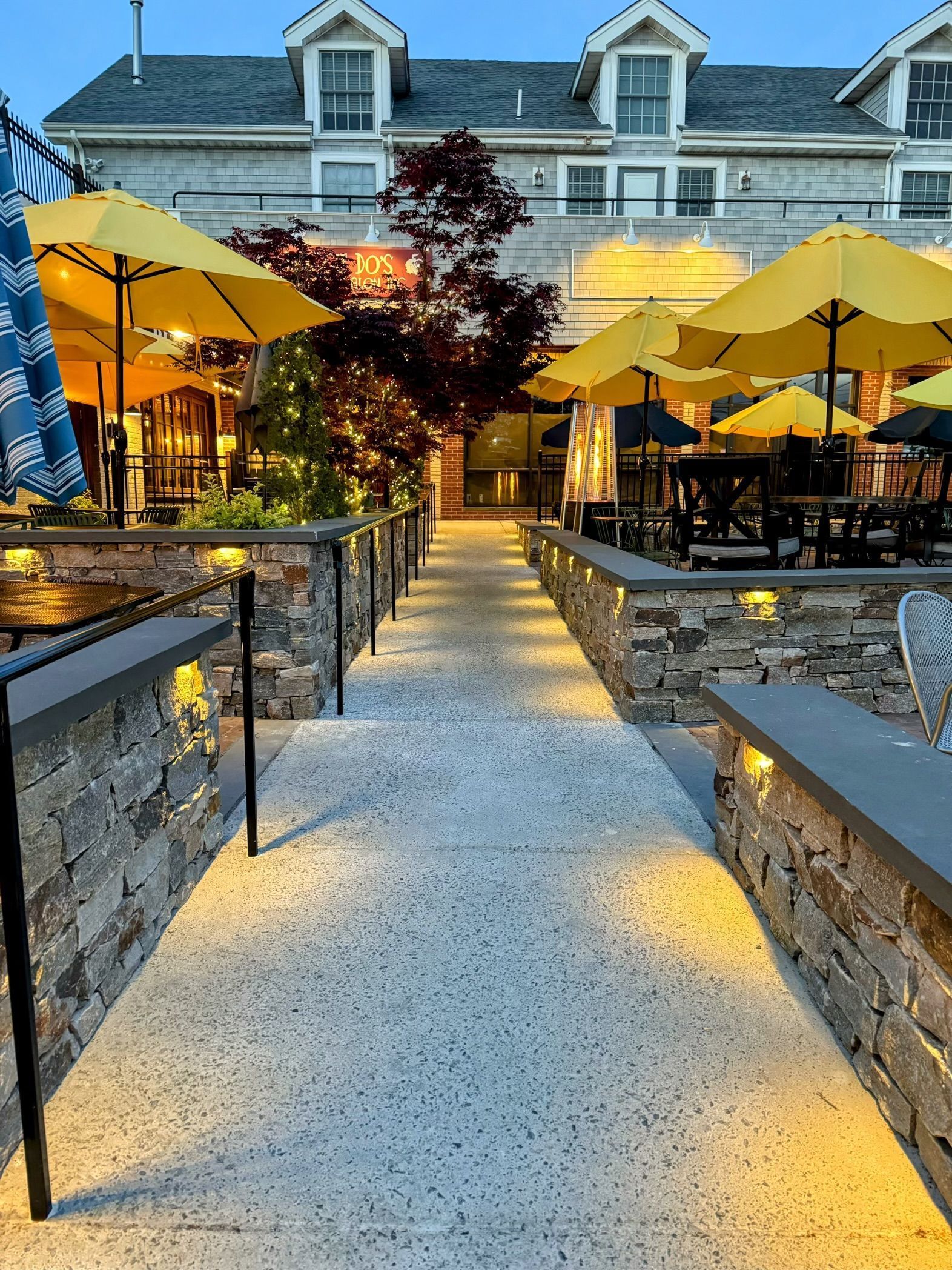 a long walkway leading to a restaurant with yellow umbrellas and chairs