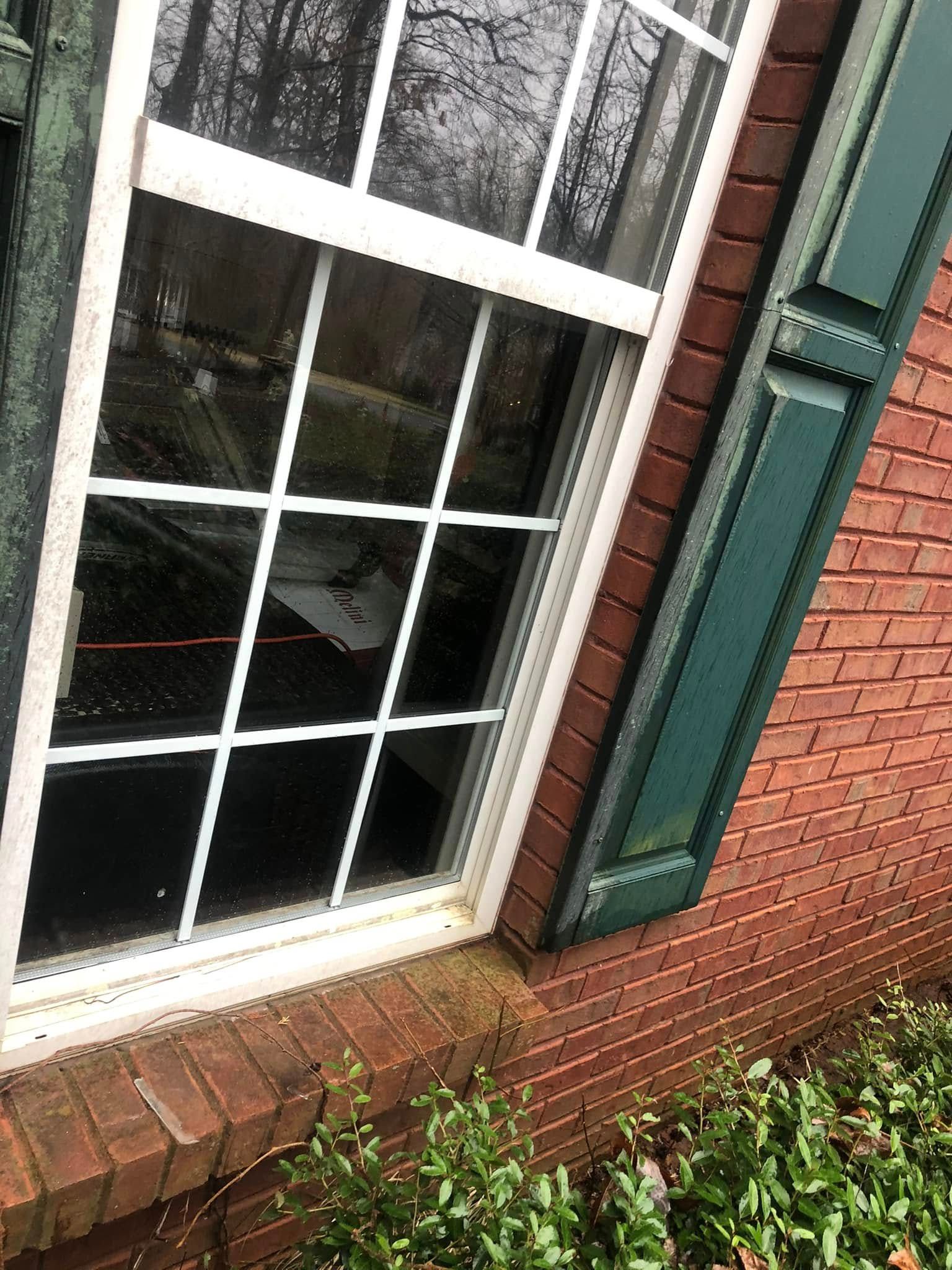 A close up of a window on a brick building with green shutters.