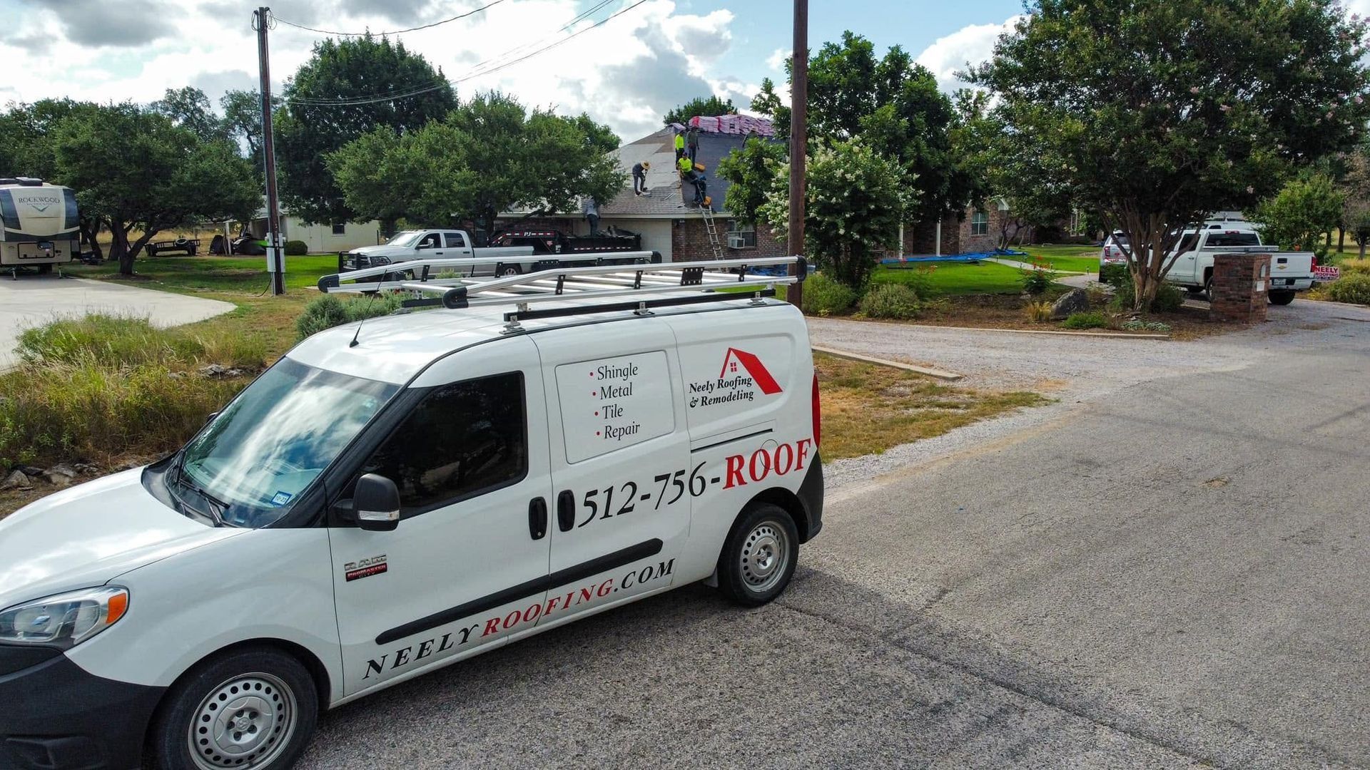 White service van with red lettering parked on a quiet residential street beside a yard and trees.