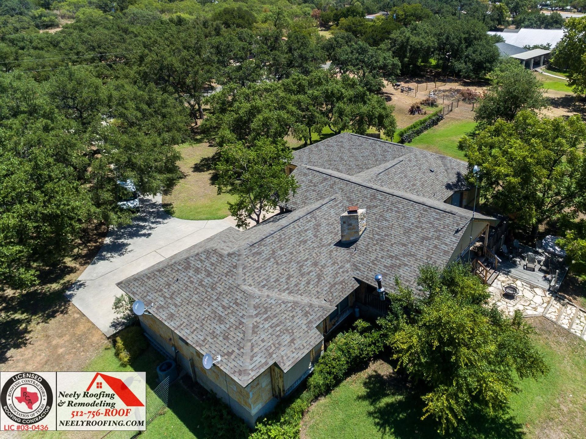 Aerial view of a gray-roofed house surrounded by green trees and a curved driveway.