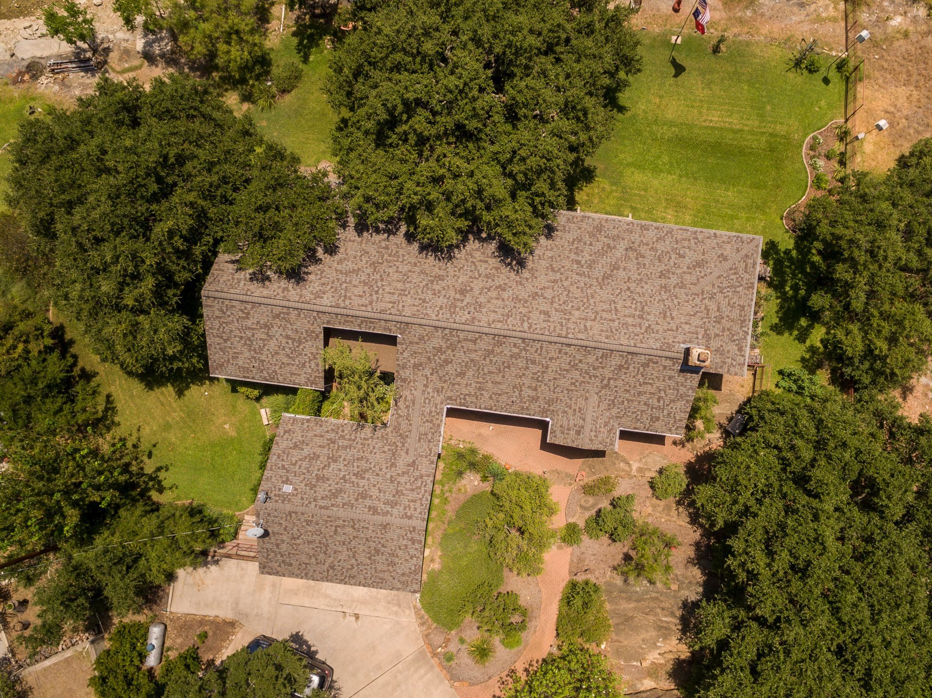 Aerial view of a house with a gray shingled roof surrounded by trees and lawn.