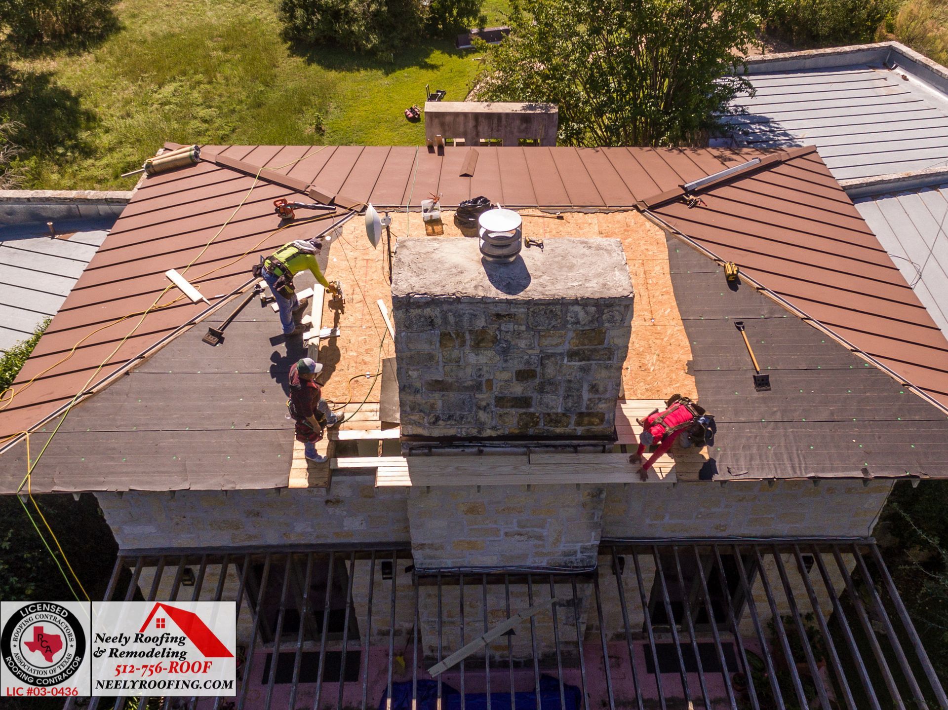 Roofers working on a house roof around a central chimney, with exposed decking and shingles.