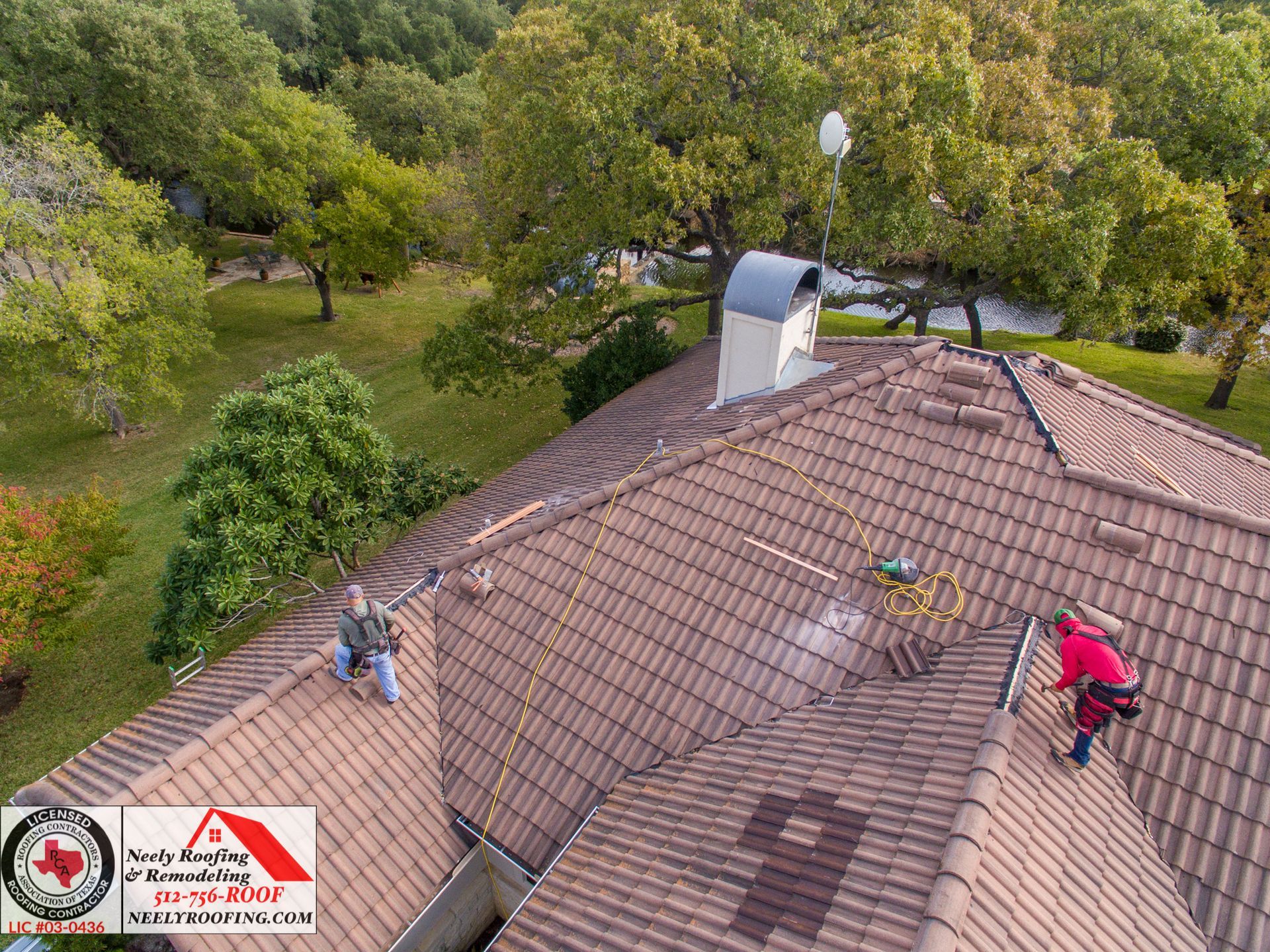Workers on a brown shingled roof in a wooded residential area, inspecting or repairing it.