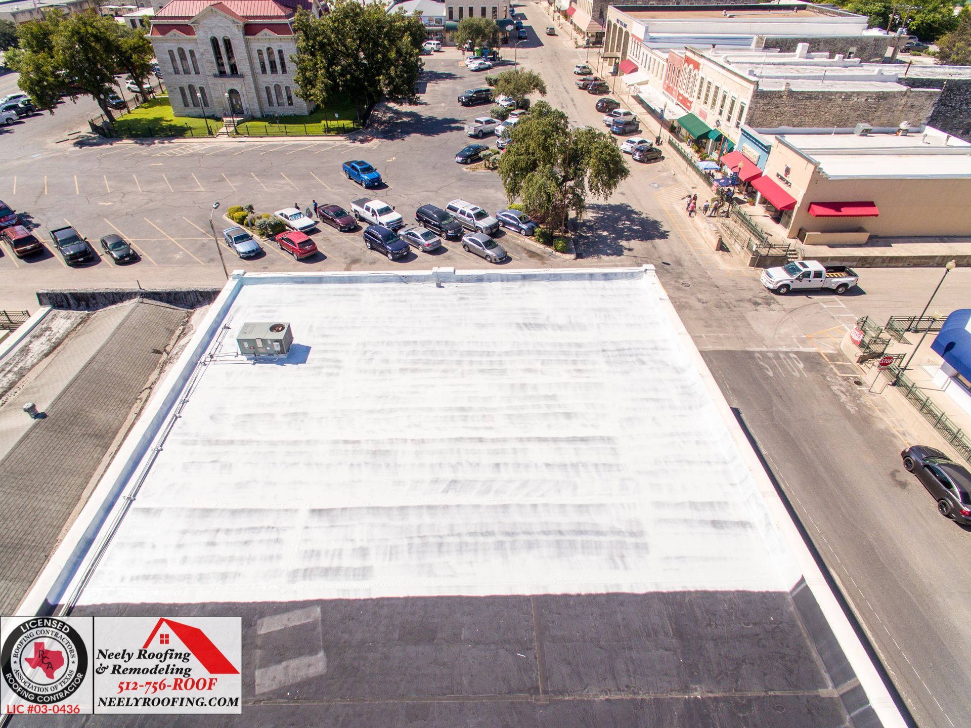 Aerial view of a white rooftop with parked cars and buildings nearby.