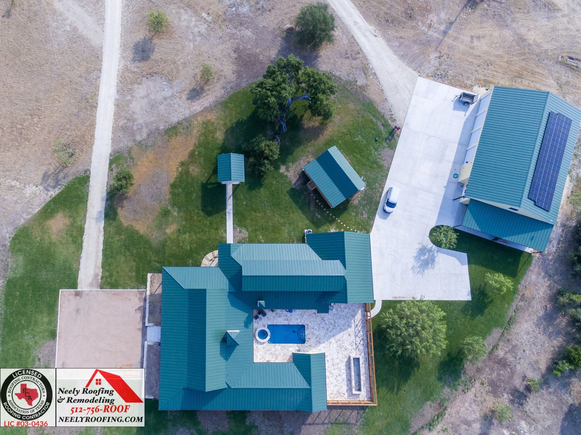 Aerial view of a small campus with teal-roofed buildings, walkways, trees, and open grassy areas.