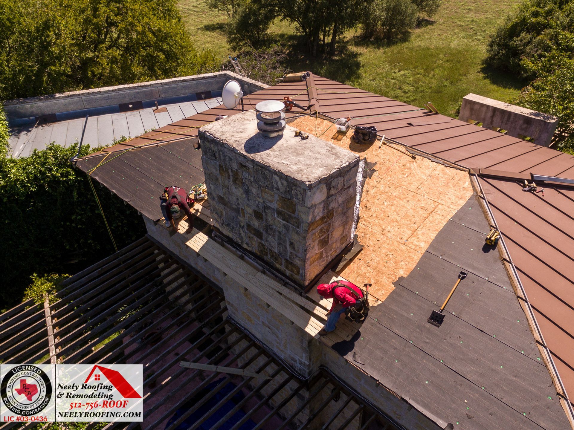 Rooftop chimney flashing repair with workers’ tools on a red metal roof and black shingle valley