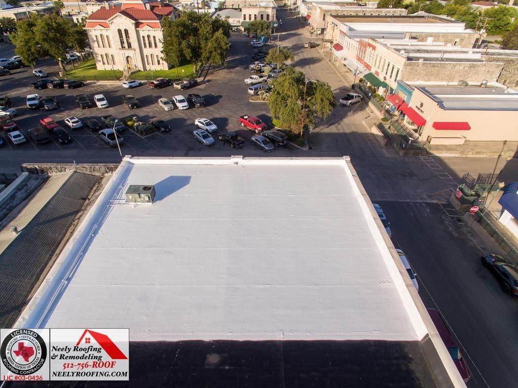 Aerial view of a large white rooftop beside a parking lot and buildings on a sunny day