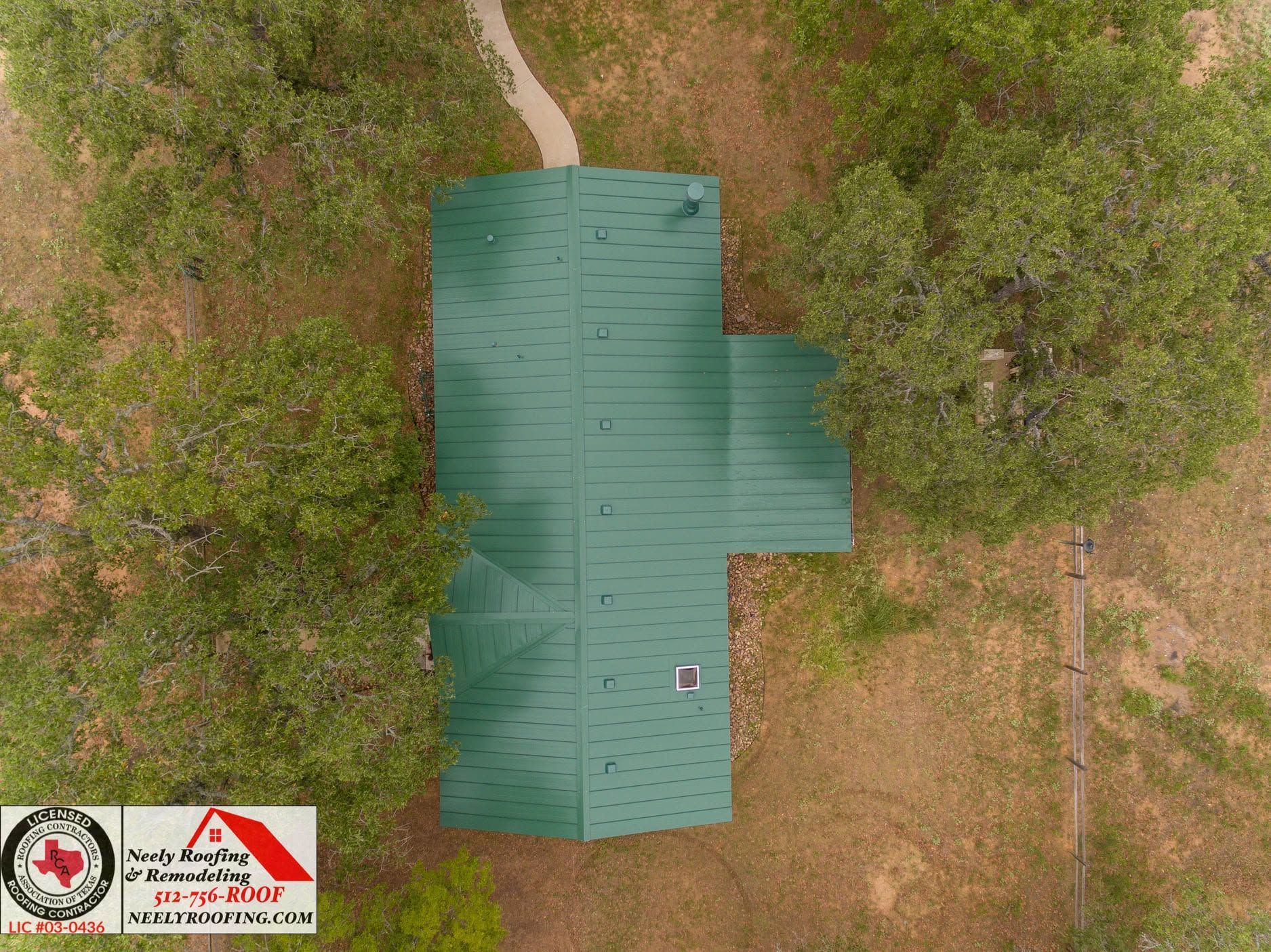 Aerial view of a green-roofed building surrounded by trees and dry grass.