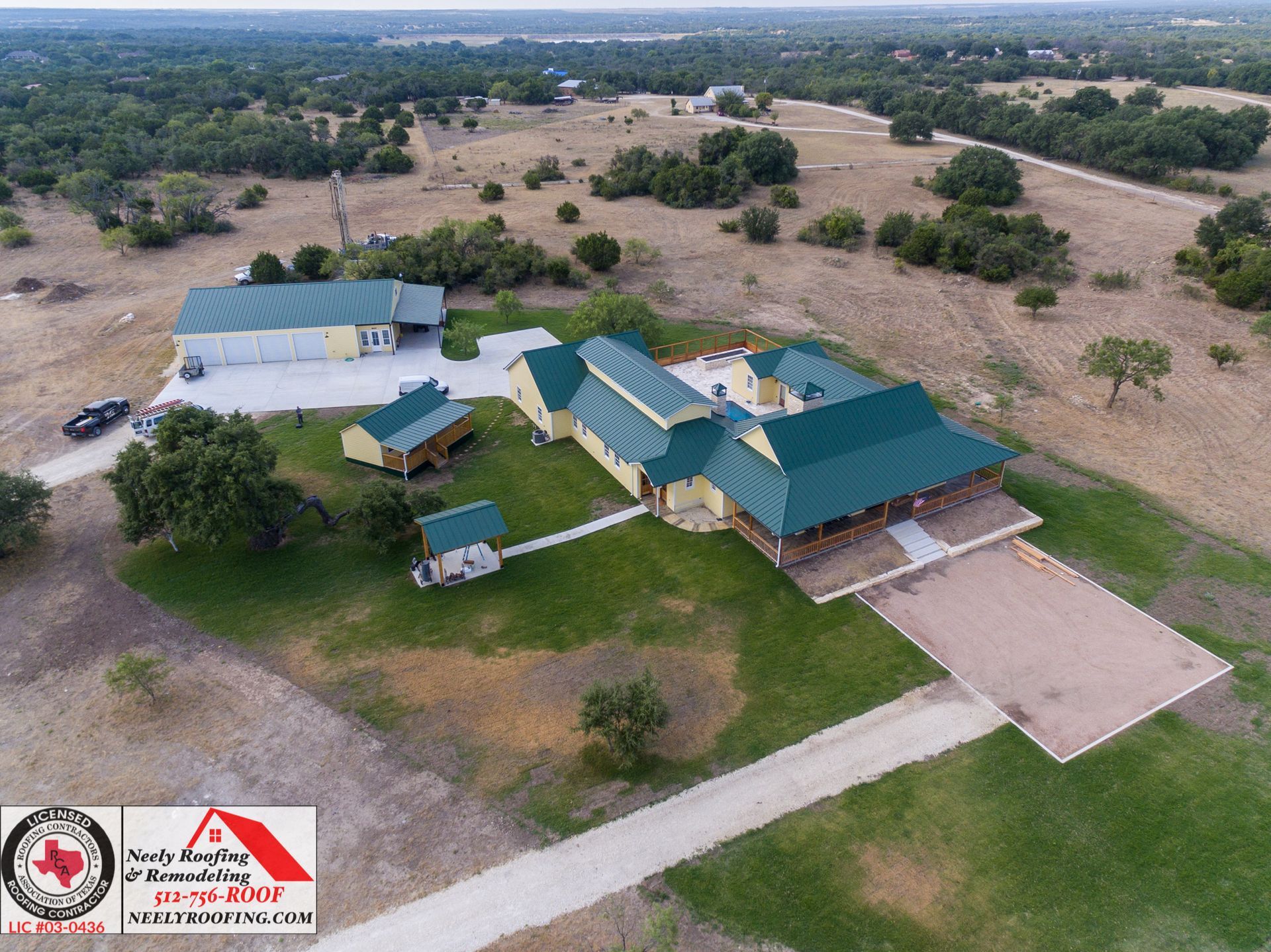 Aerial view of a rural property with green-roofed buildings, paved driveway, and open fields.
