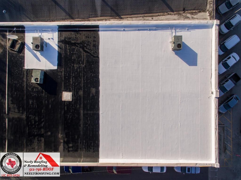 Aerial view of a flat roof with white and black sections, HVAC units, and parked cars along one side.