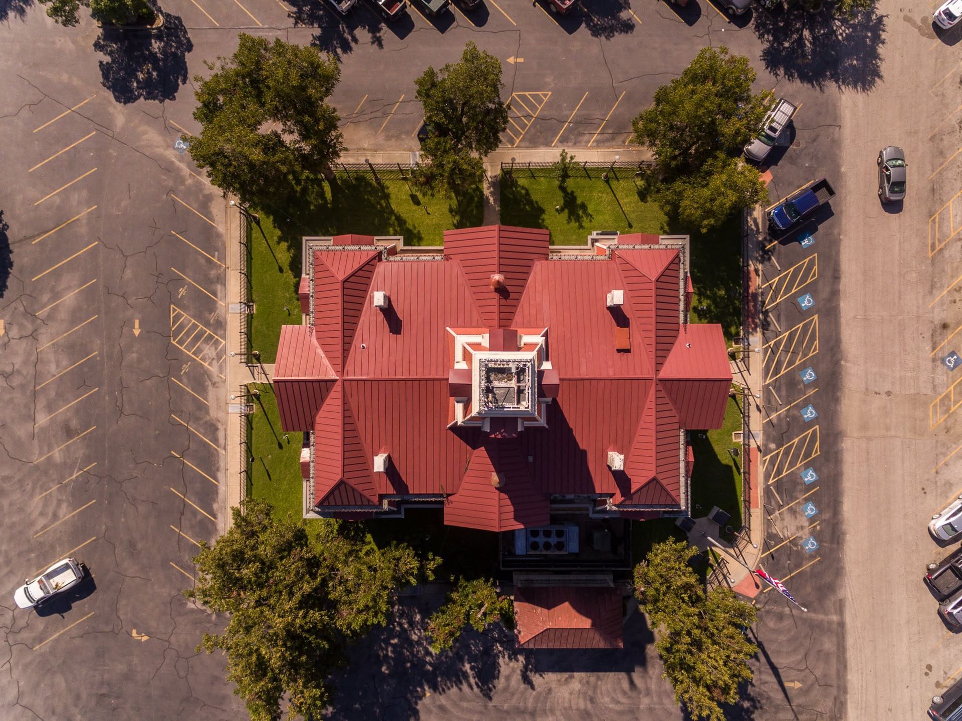 Aerial view of a red-roofed building surrounded by trees and an empty parking lot.