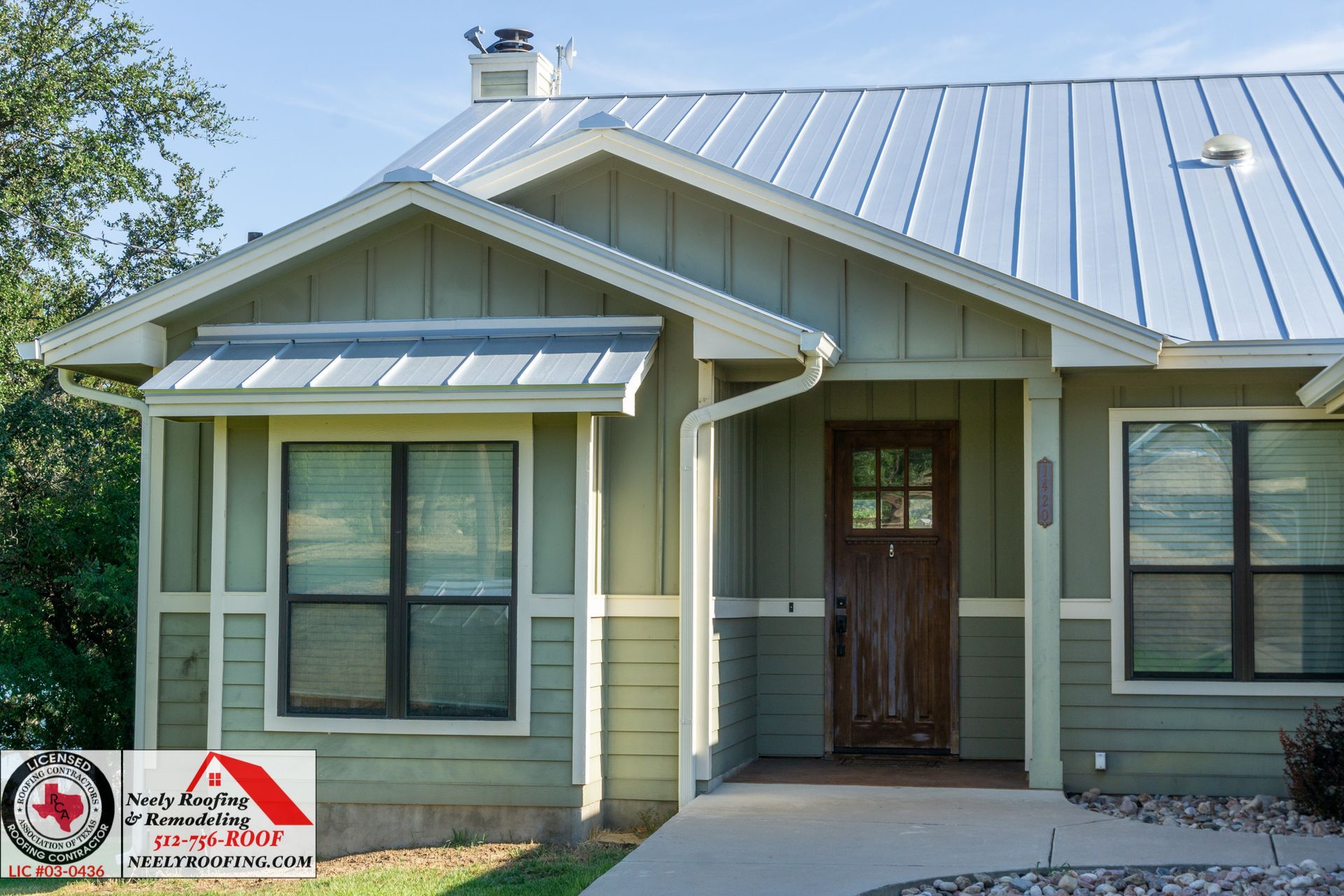 Single-story green house with metal roof, front porch, and large windows.