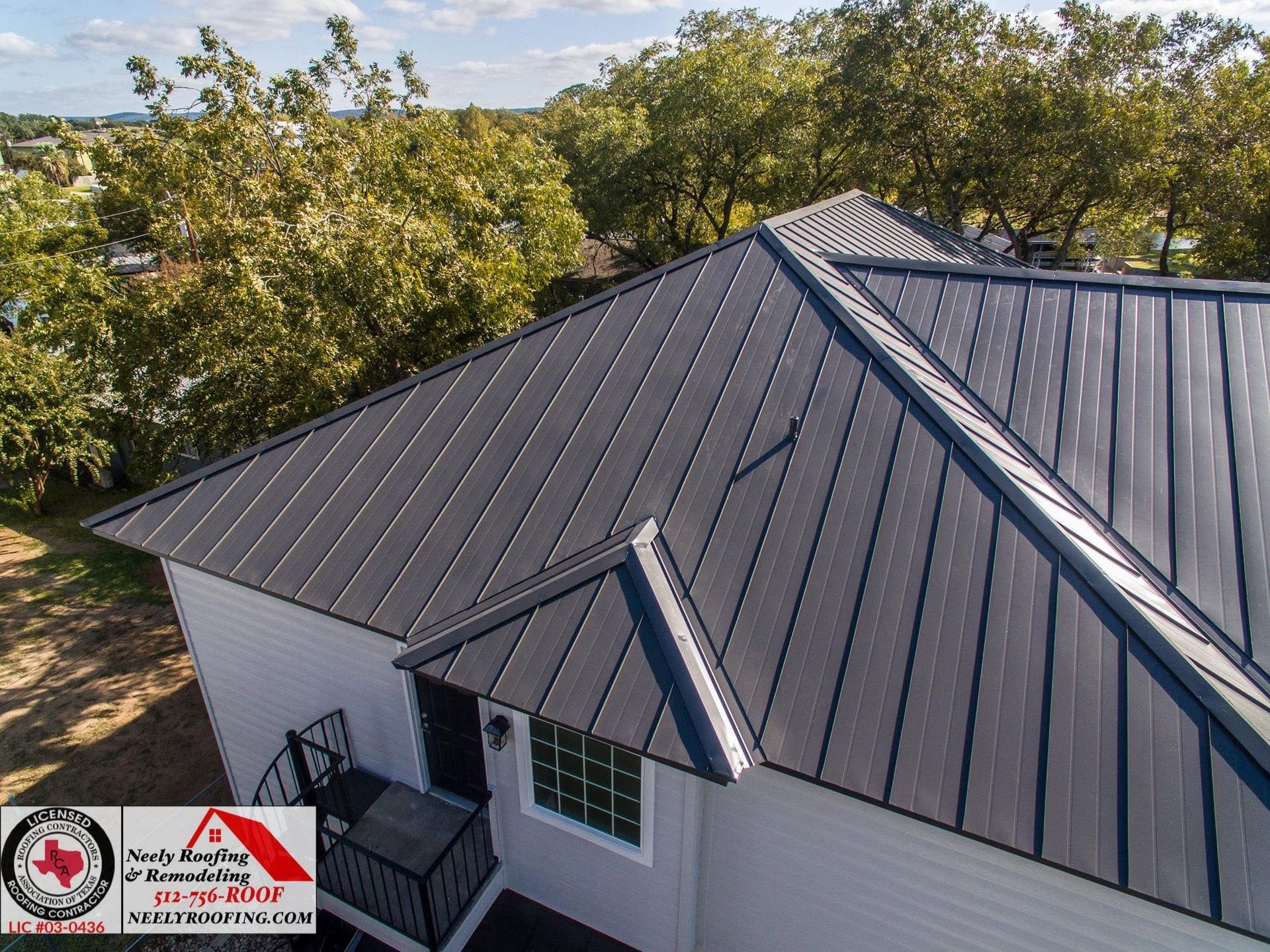 Aerial view of a gray metal roof with dormer and trees in the background