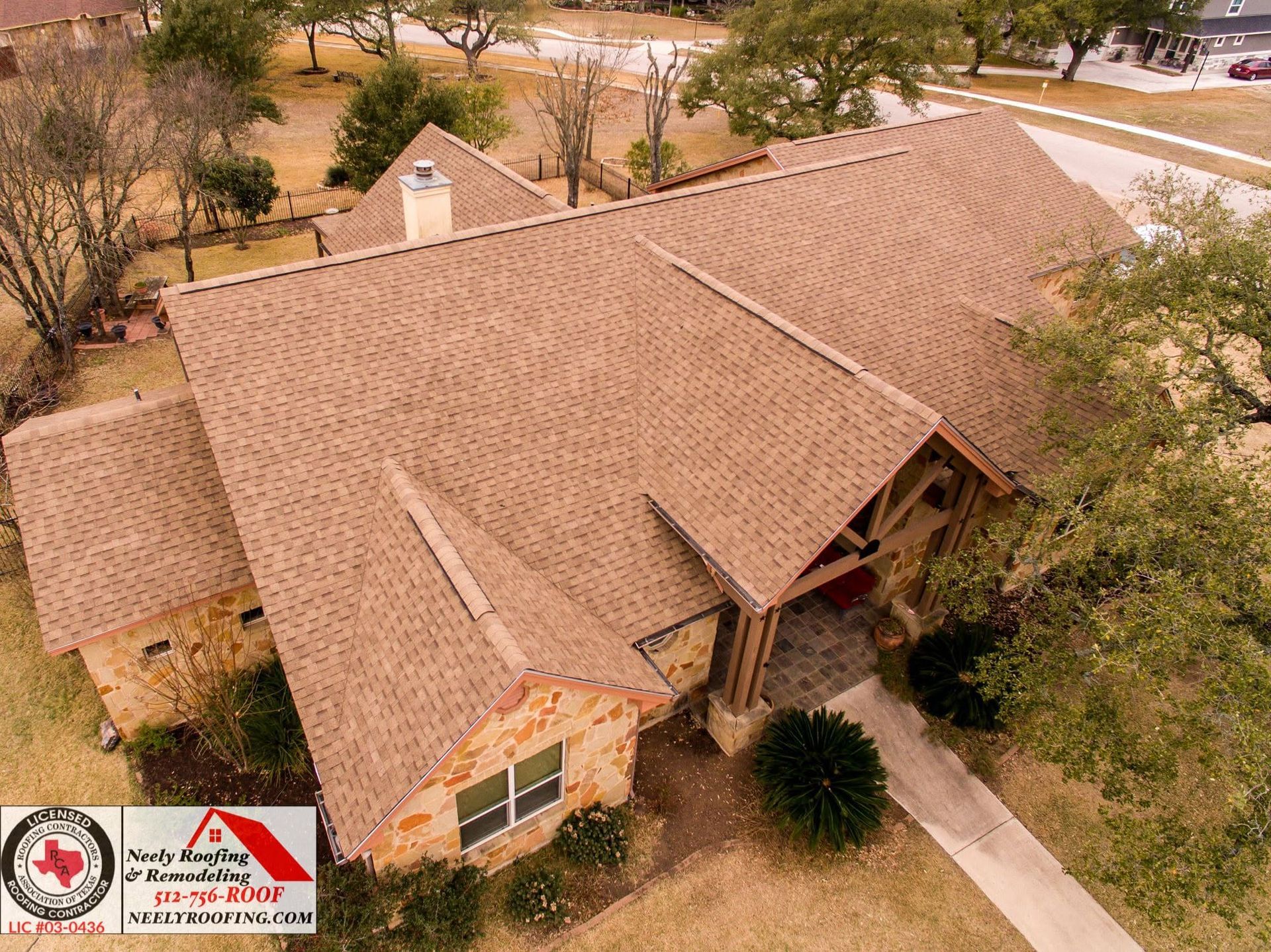 Aerial view of a tan shingle-roof house with a front porch and surrounding trees on a dry lot