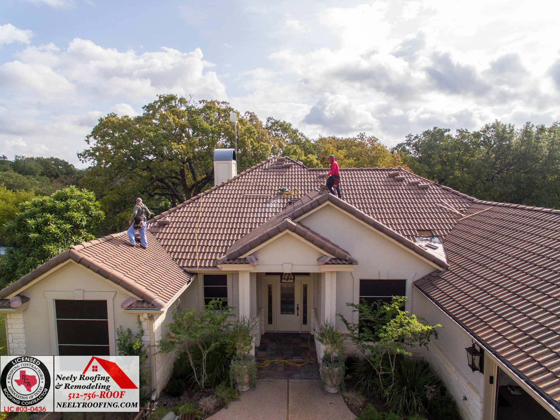 Aerial view of a house with two workers on the roof, surrounded by trees and cloudy sky.