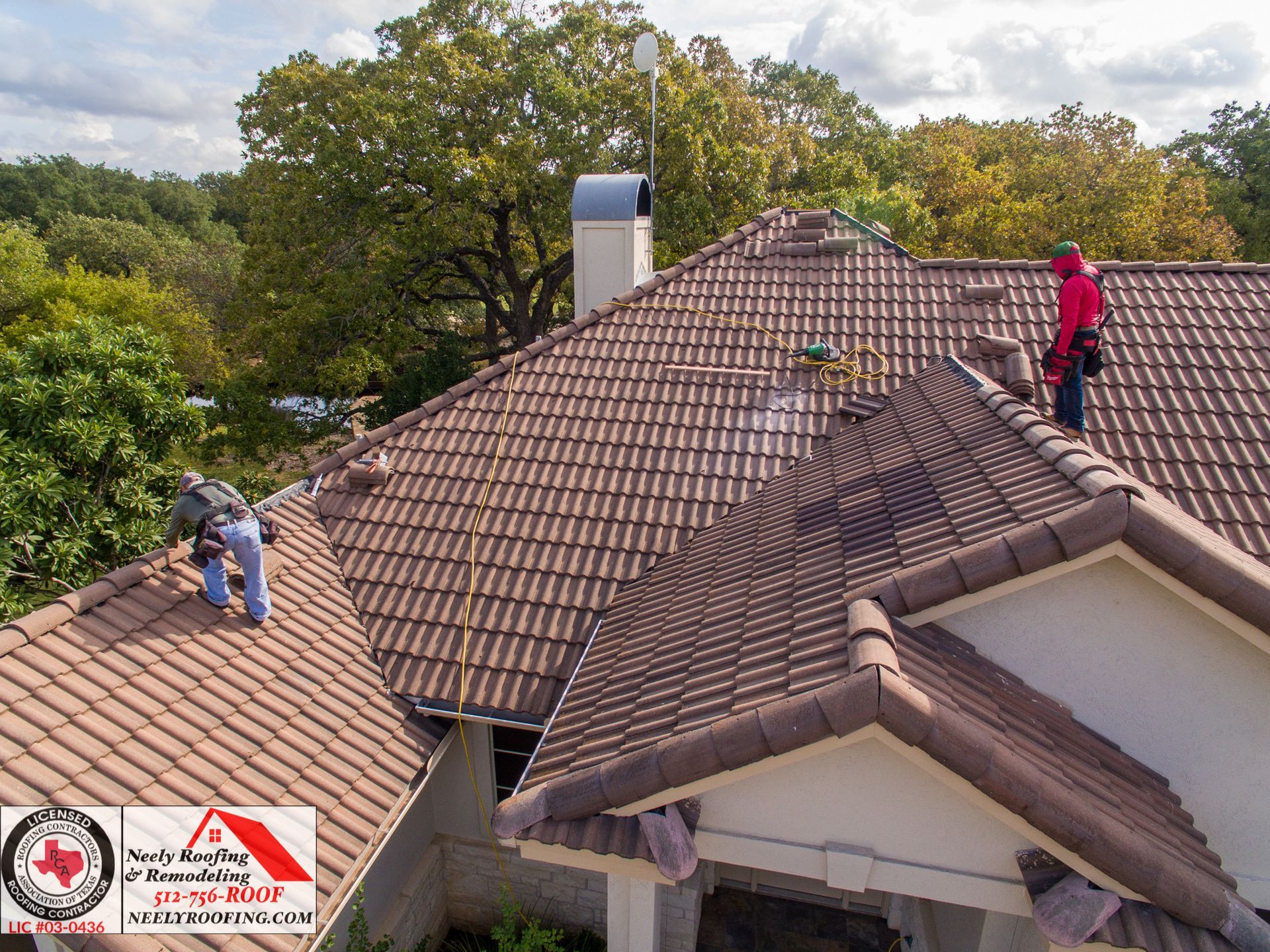 Two workers inspecting a tiled roof with trees in the background