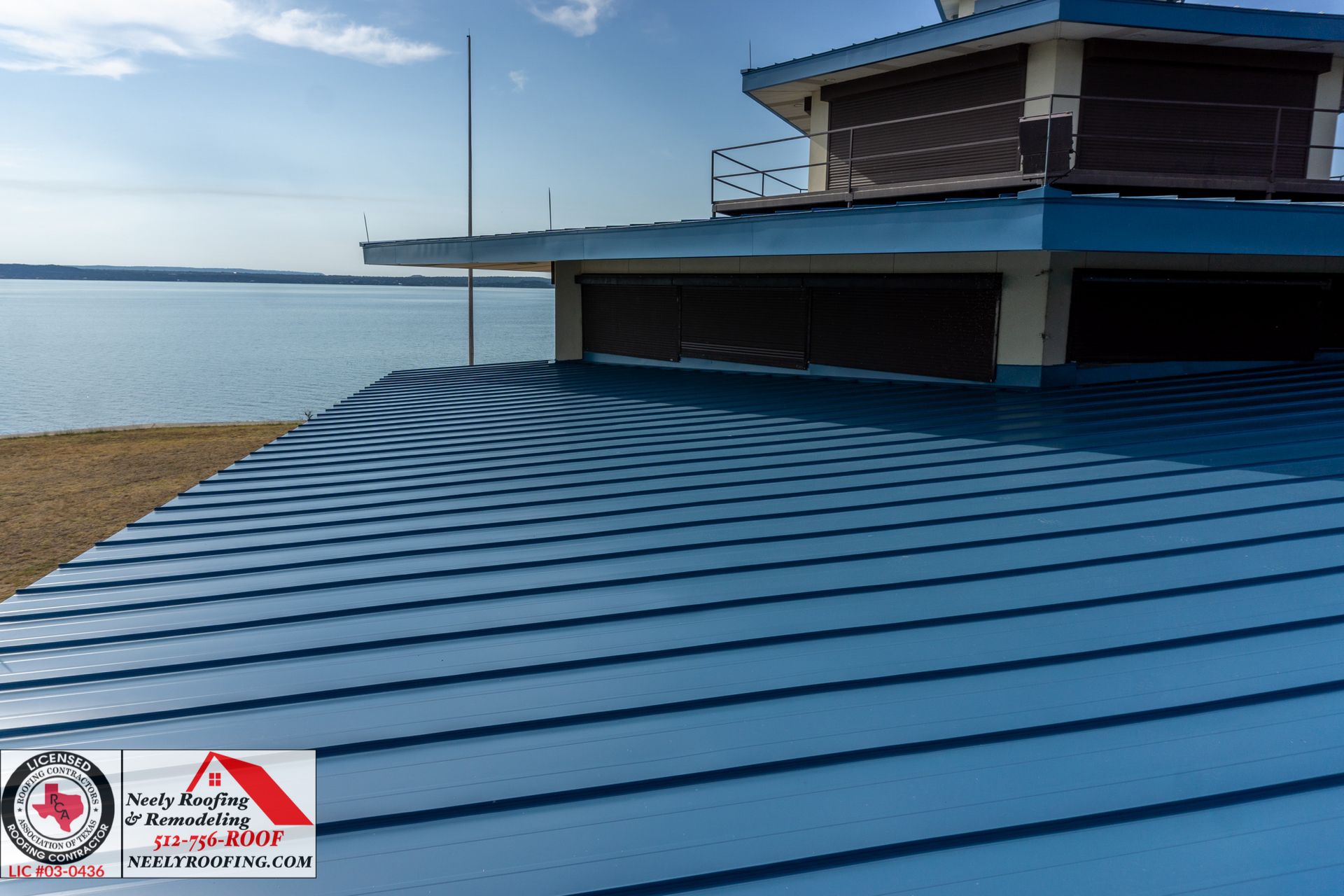 Blue metal roof beside calm water under a clear sky, with a building deck extending over the shoreline.