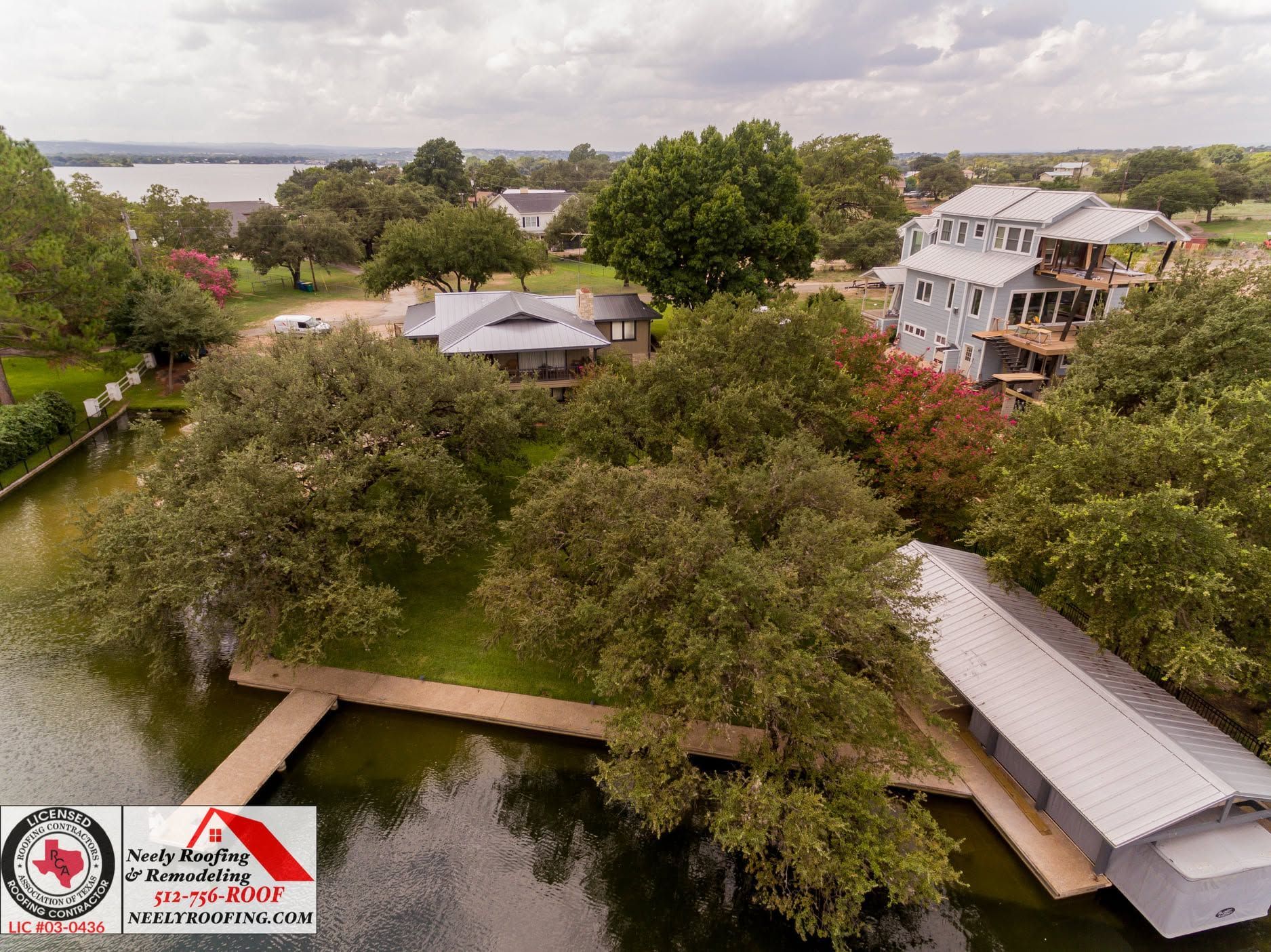 Aerial view of a tree-lined canal with houses, a small bridge, and a dock under cloudy skies