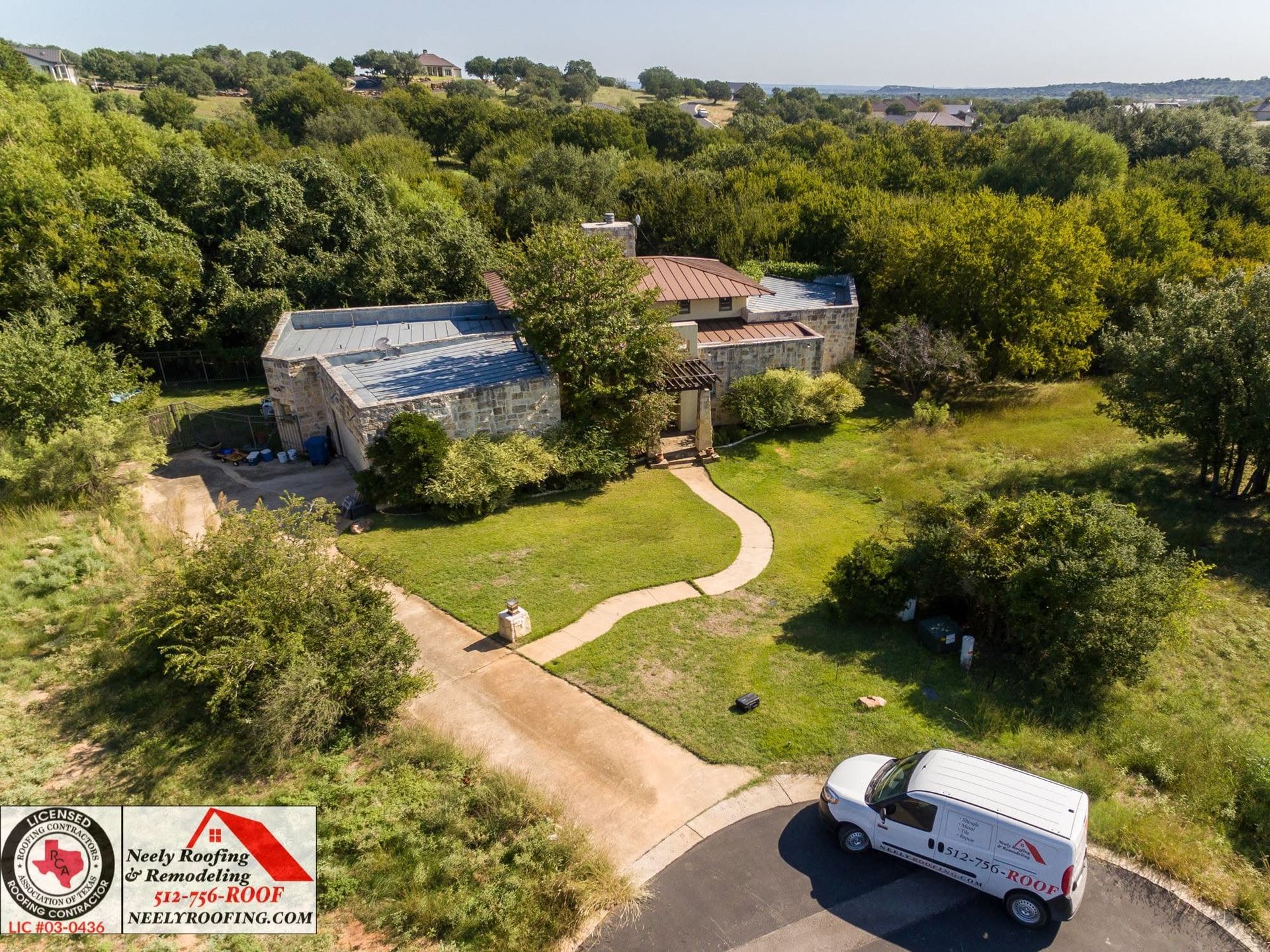 Aerial view of a rural property with two buildings, a curved dirt path, trees, and a parked white van.