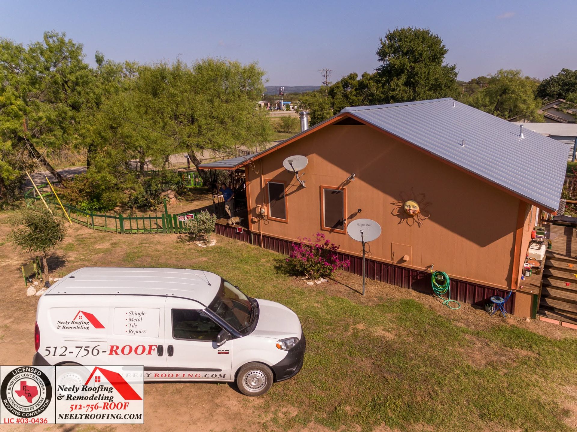 White service van parked beside a brown house with a silver roof and satellite dishes in a grassy yard.