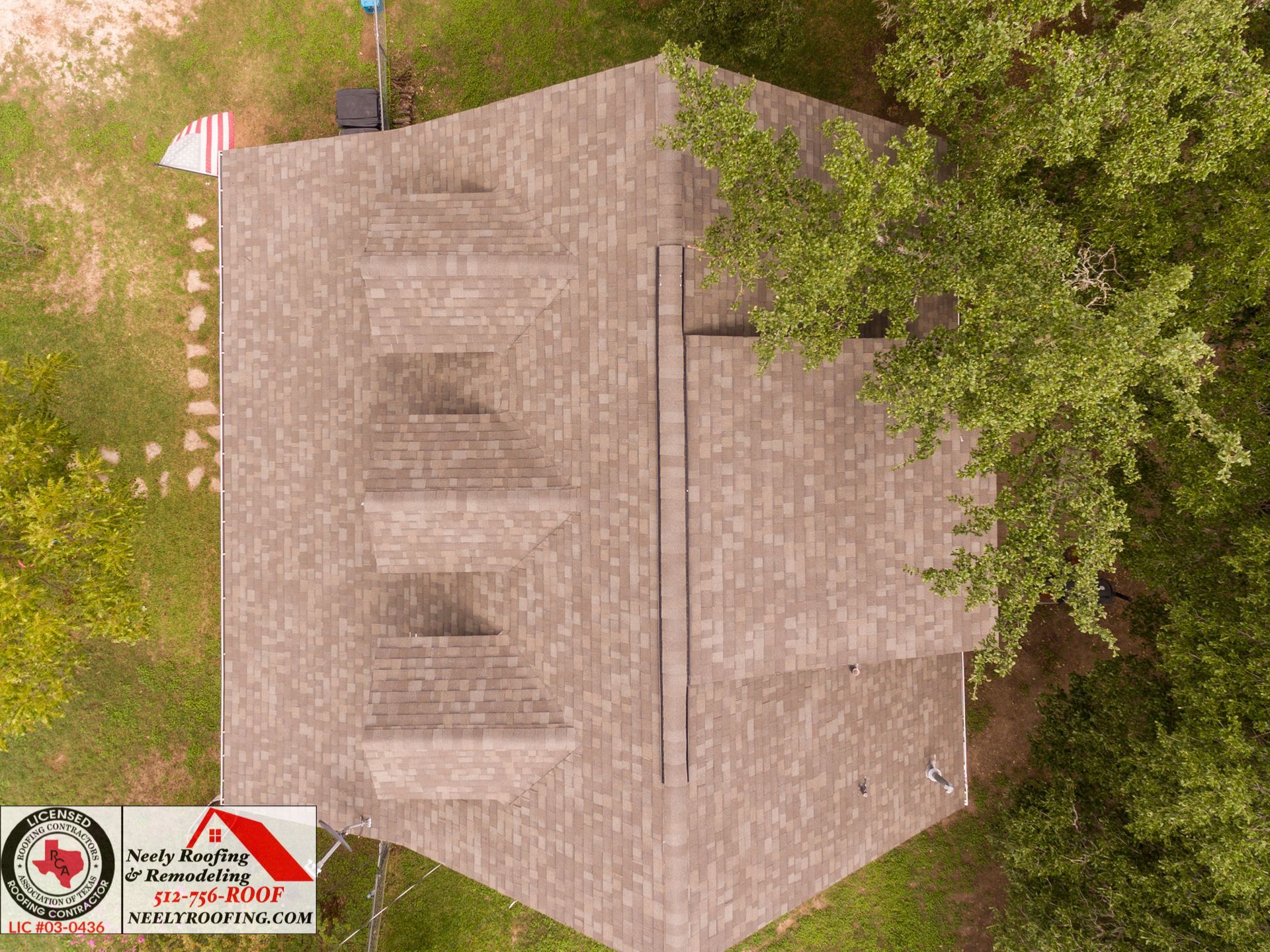 Overhead view of a small beige-roofed building beside trees, with a paved area and signs in the corner
