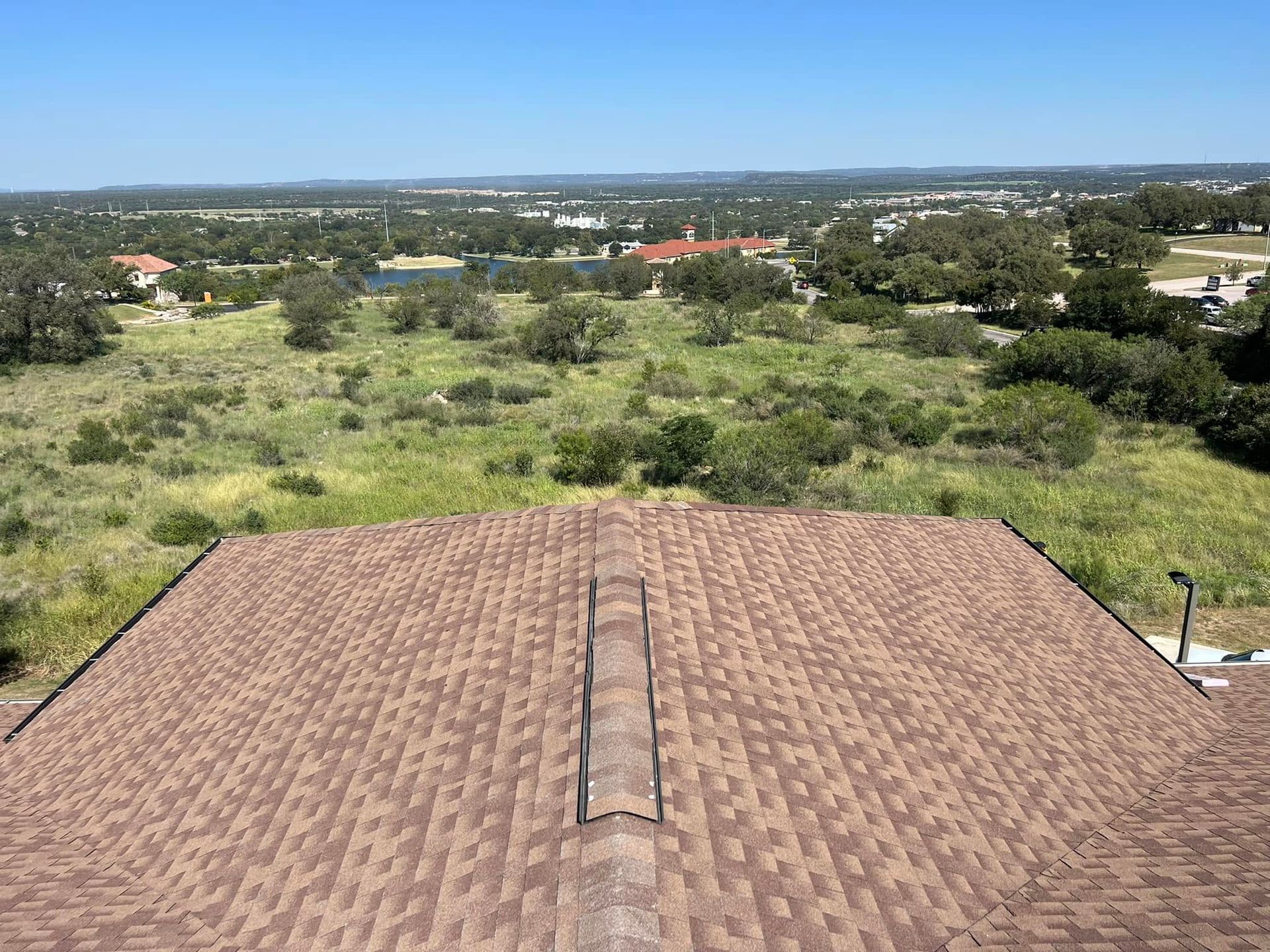Rooftop overlooking a green field and distant houses under a clear blue sky