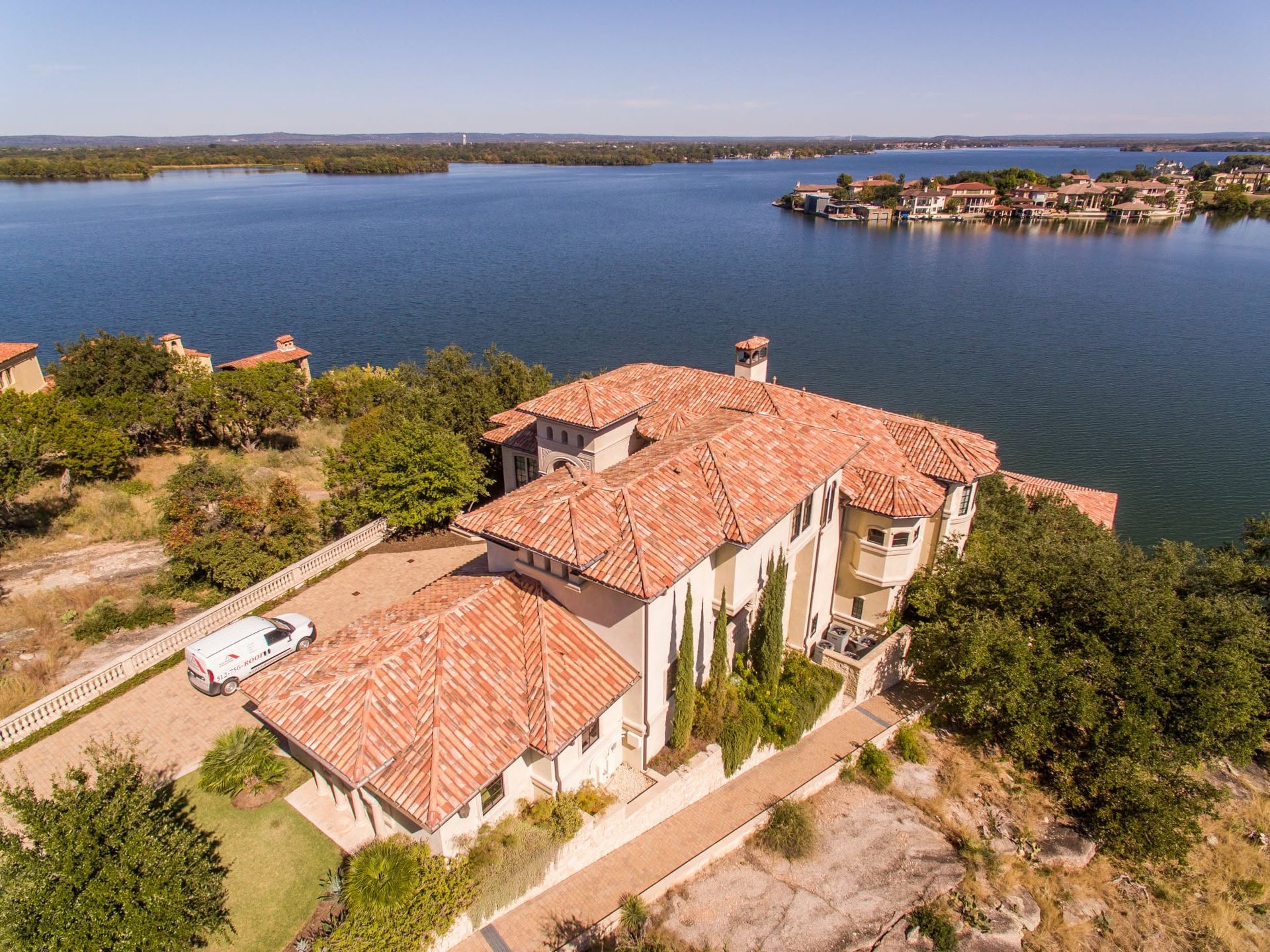 Aerial view of a terracotta-roofed villa by a large lake with a small island in the distance