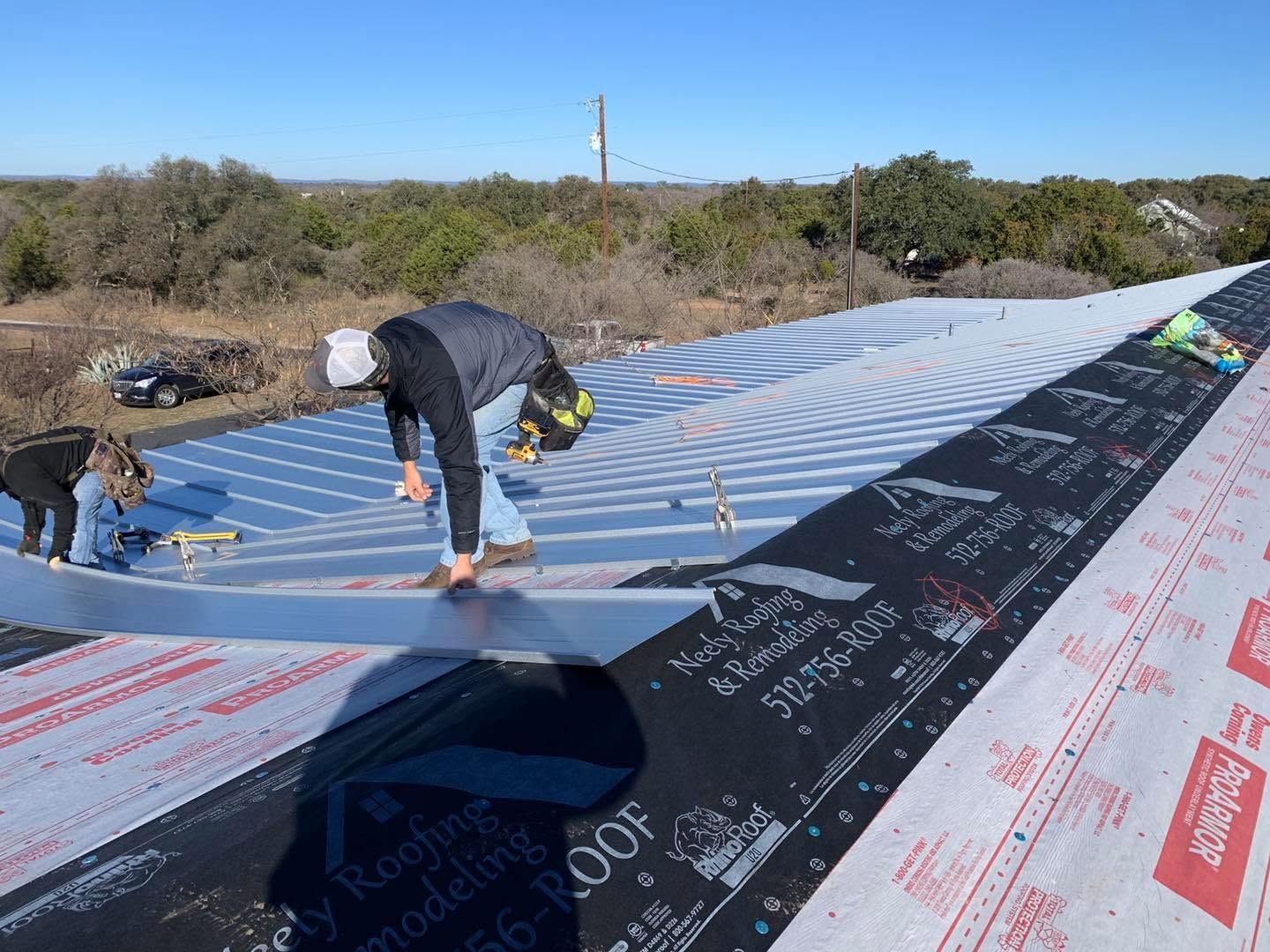 Workers installing roofing underlayment on a sloped roof on a sunny day