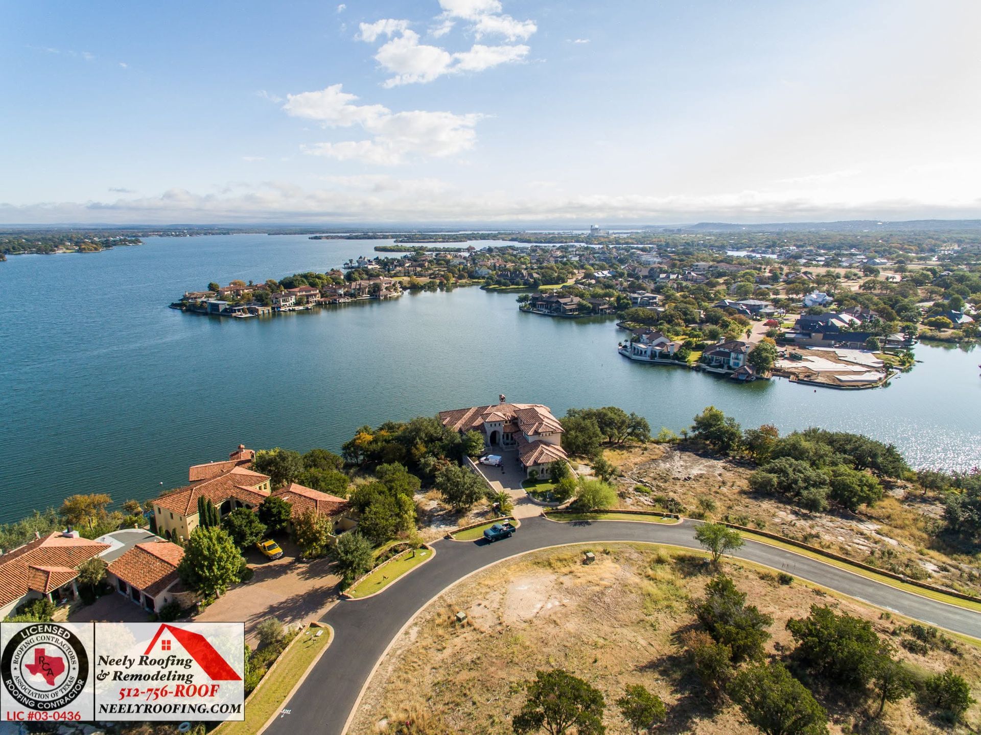 Aerial view of a coastal lakeside town with blue water, scattered islands, and winding roads under a bright sky