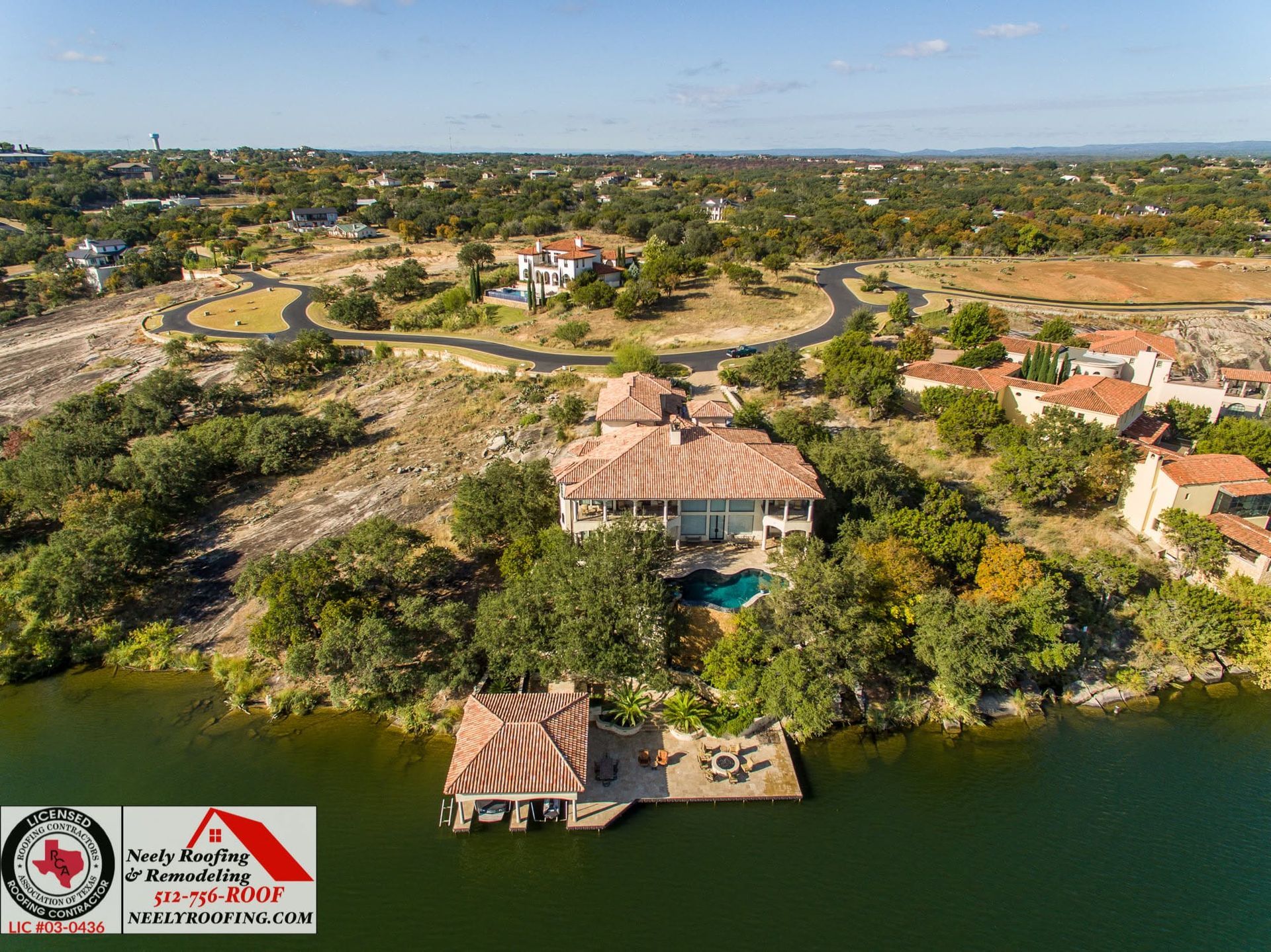 Aerial view of a riverside neighborhood with homes, winding roads, and green trees.
