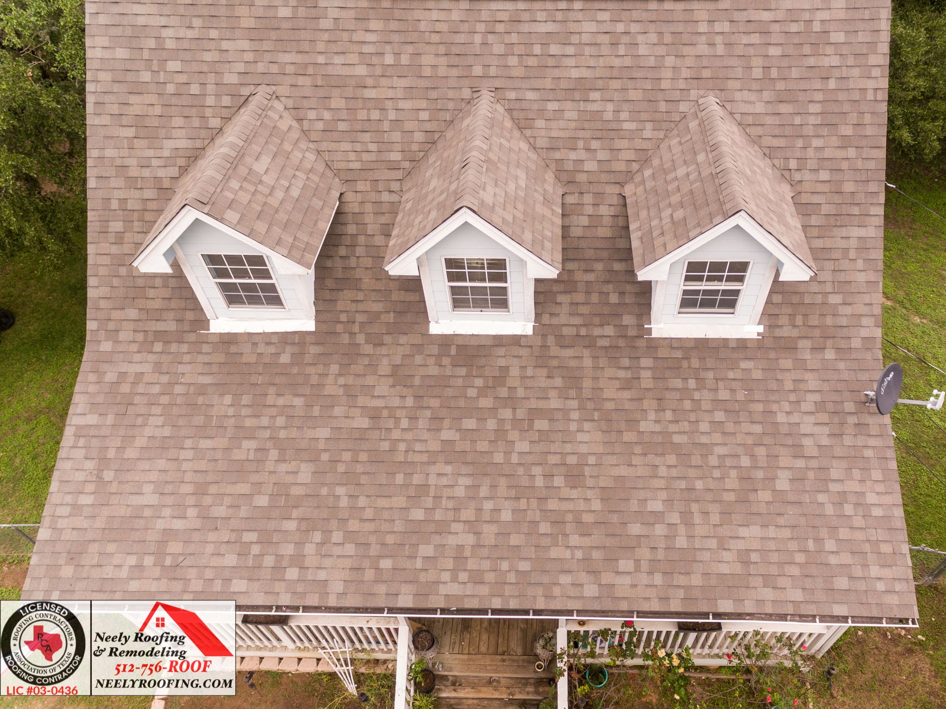 Aerial view of a shingled house roof with three dormer windows and a small logo watermark in the corner