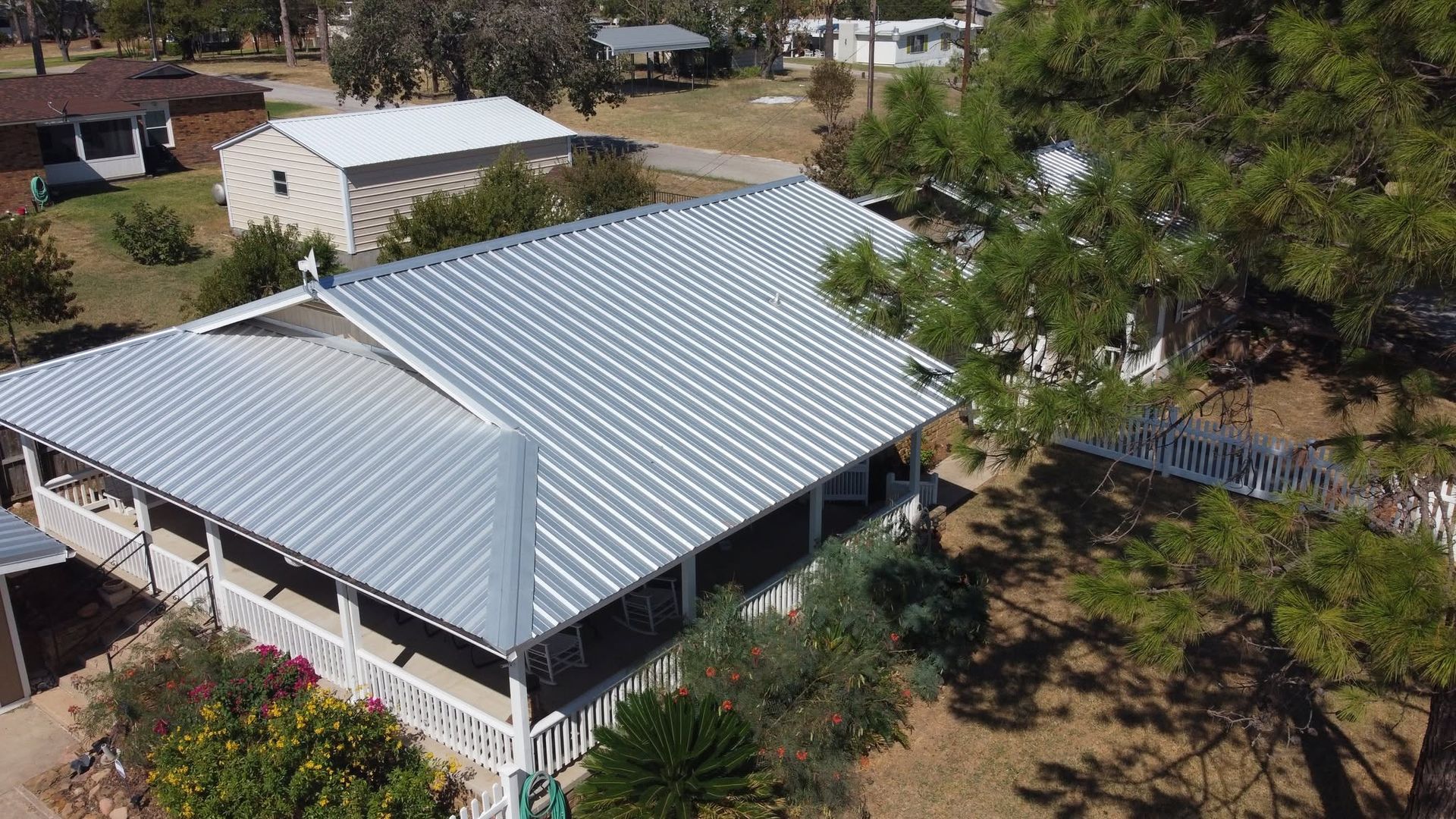Aerial view of a house with a gray metal roof surrounded by trees and yard.