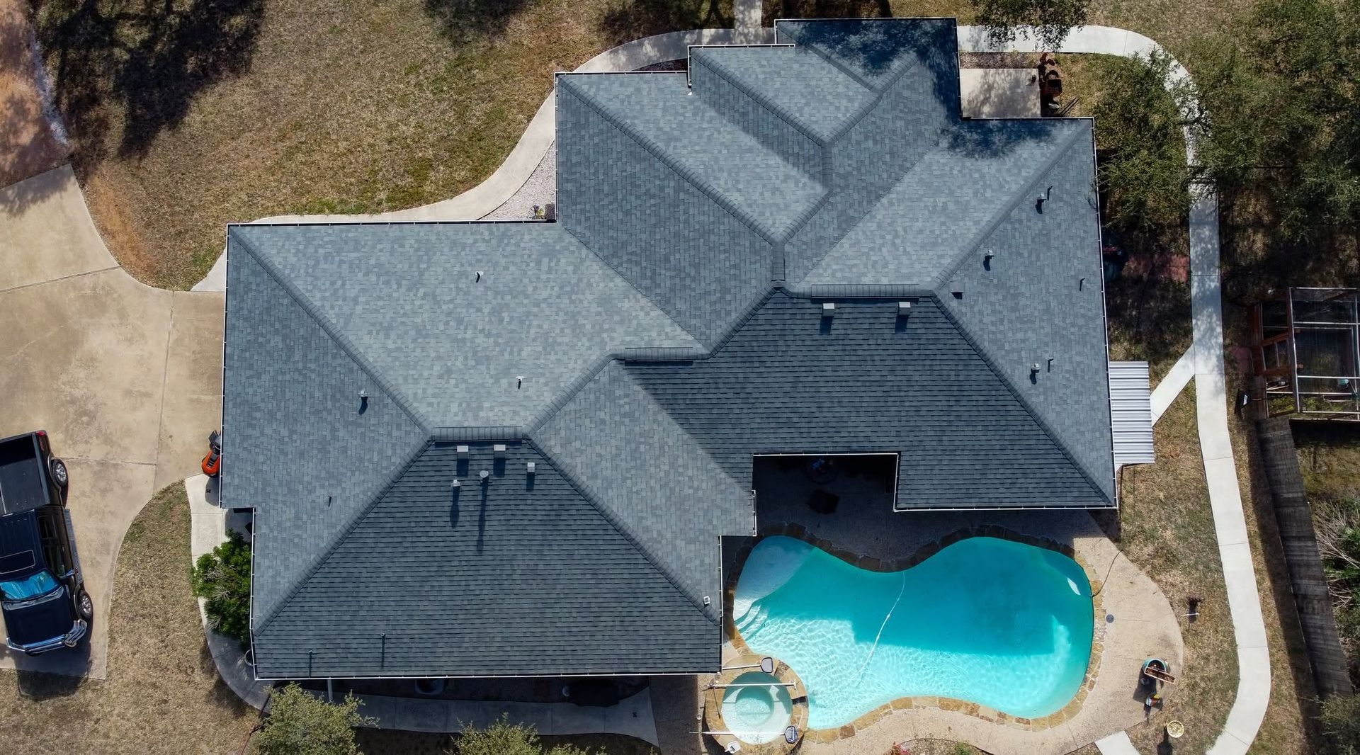 Aerial view of a gray-roofed house with a turquoise backyard pool.