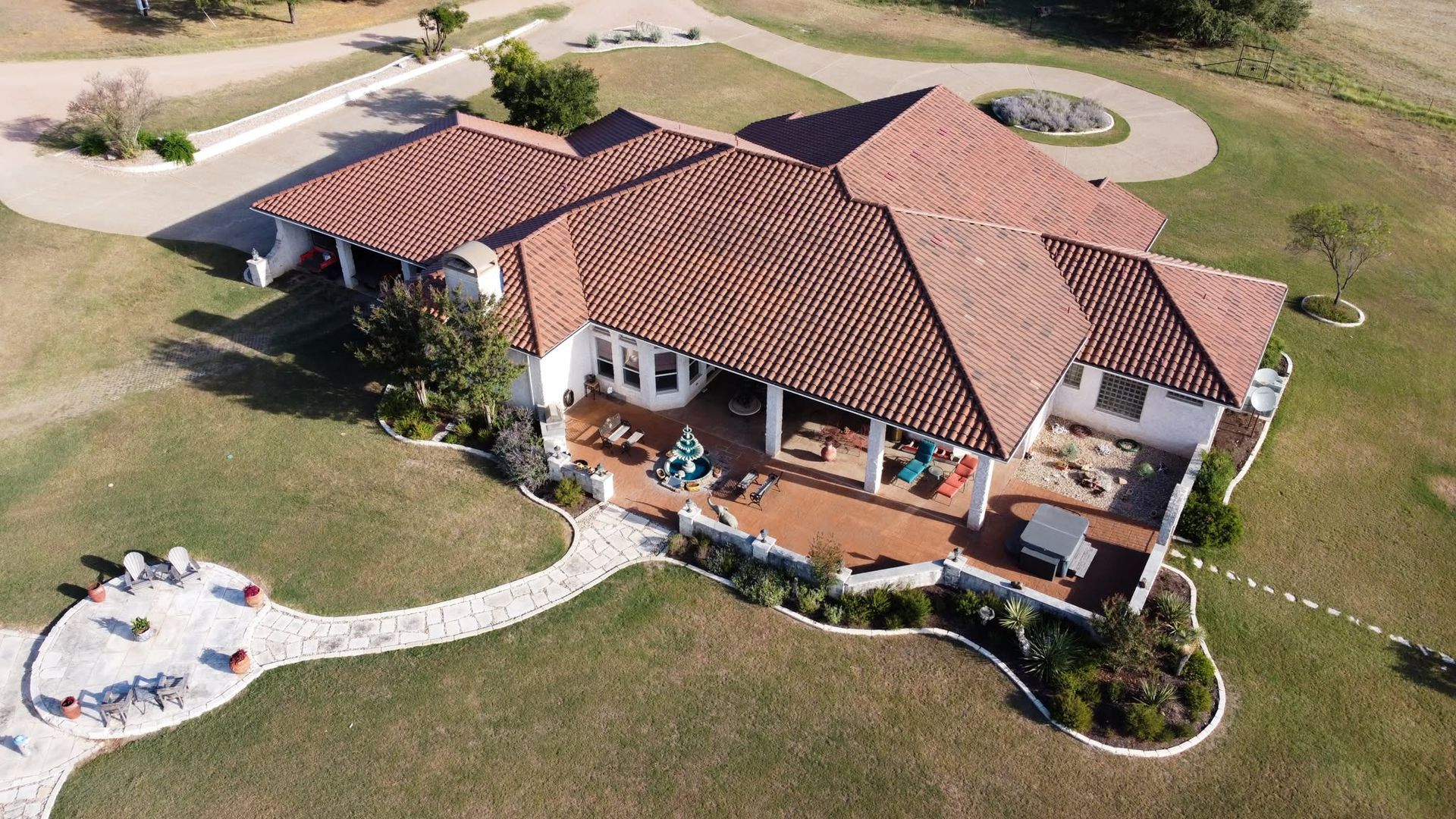 Aerial view of a tan house with a red tile roof, curved walkway, and lawn in a suburban yard